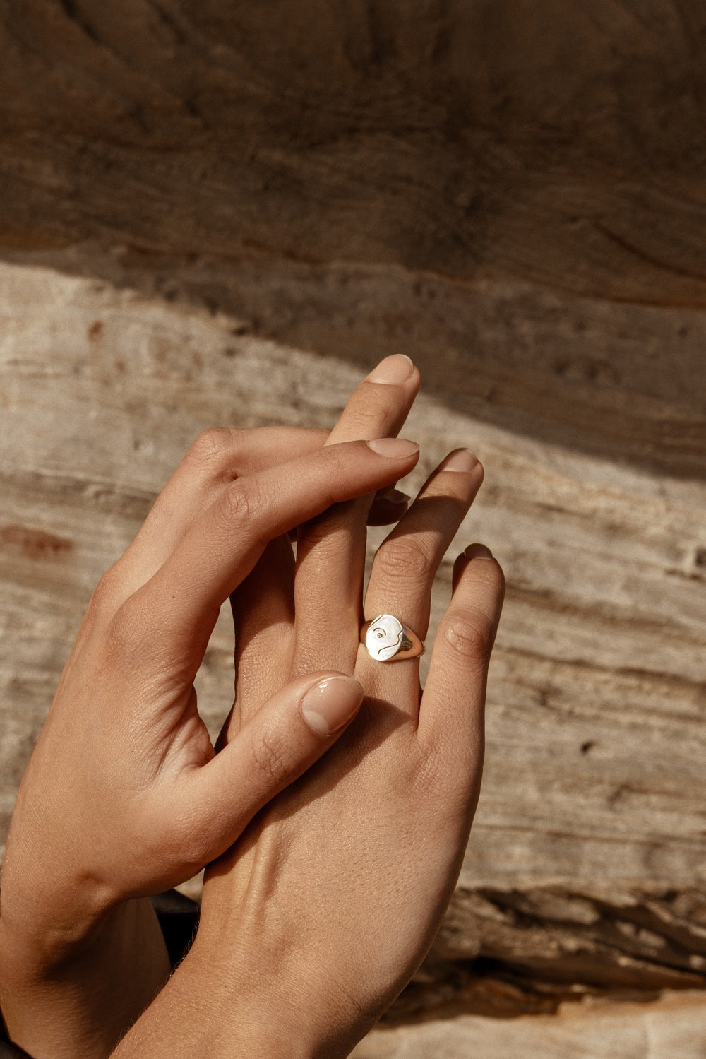 Hands with a gold ring featuring a round face and delicate engraving, set against a rustic wooden background. High-end jewellery, elegance.