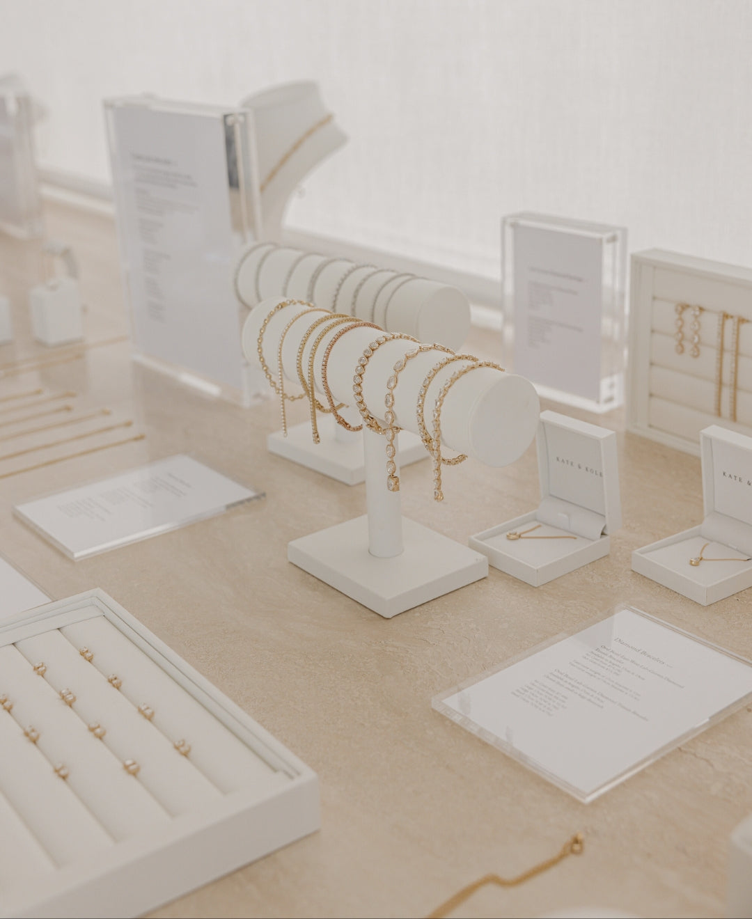 Luxury jewellery display with gold bracelets, necklaces, and rings on a beige countertop. Elegant presentation in a minimalist setting.