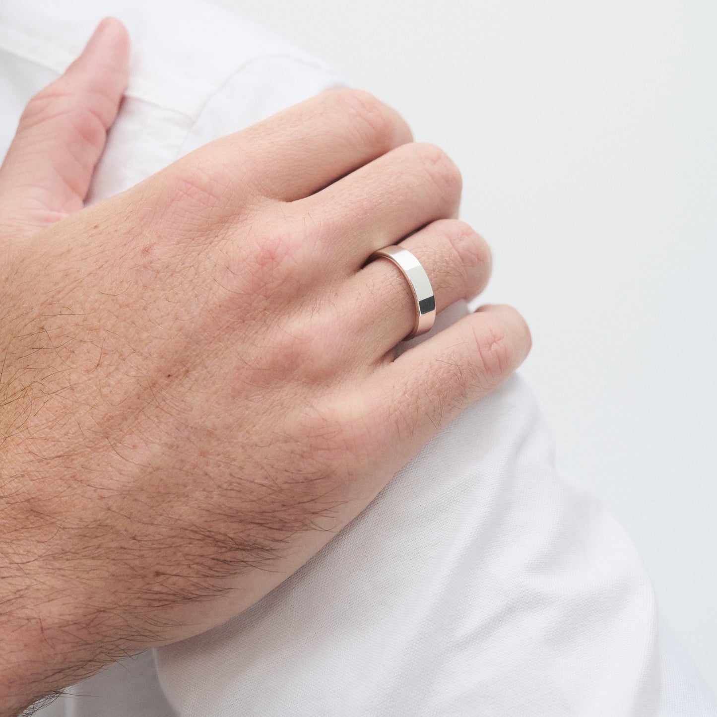 A close-up of a hand wearing a sleek, polished gold ring, resting on a white fabric, showcasing luxury jewellery and minimalist design.