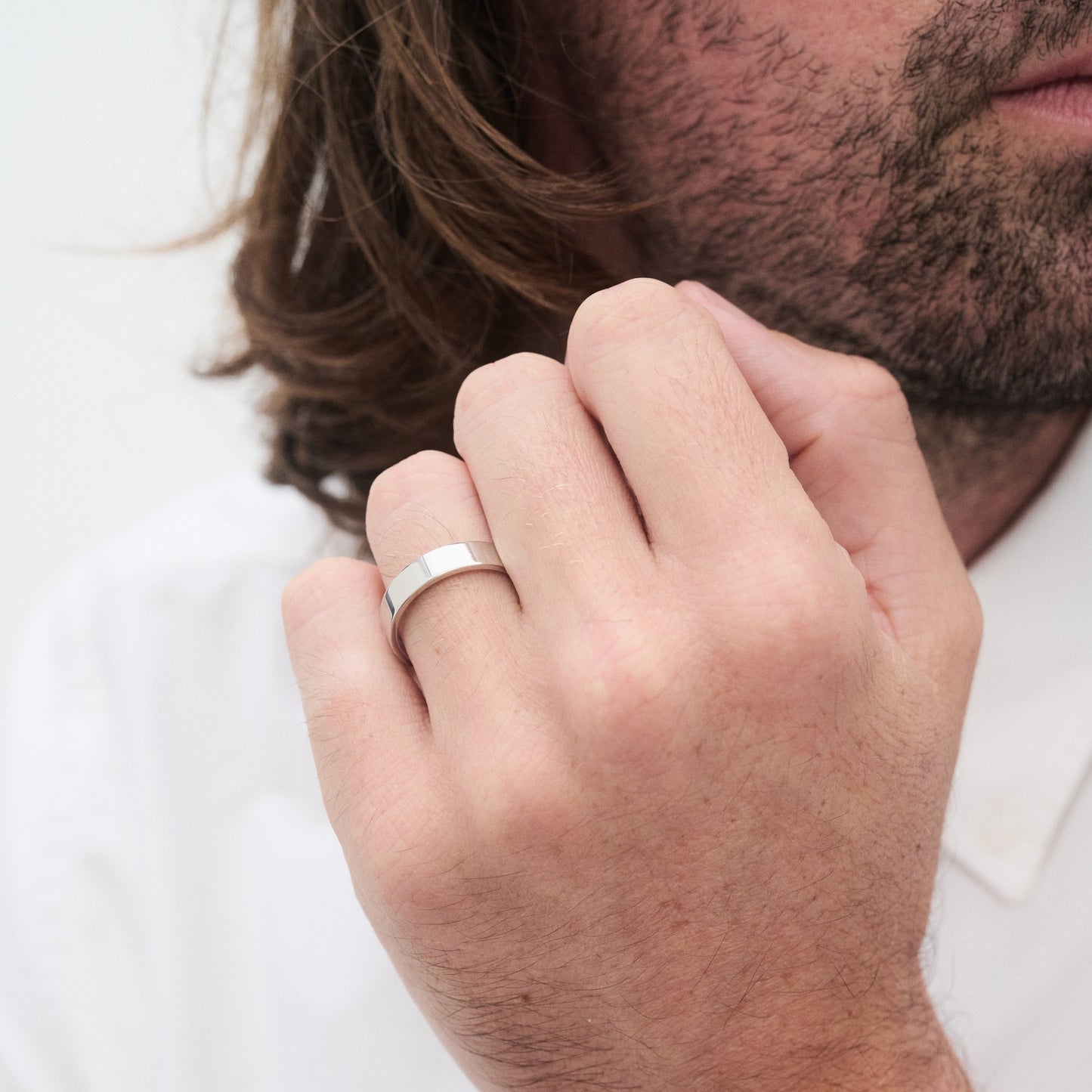 Man wearing a silver band ring on his finger, with a focus on the hand and ring. He has a beard and wears a white shirt.