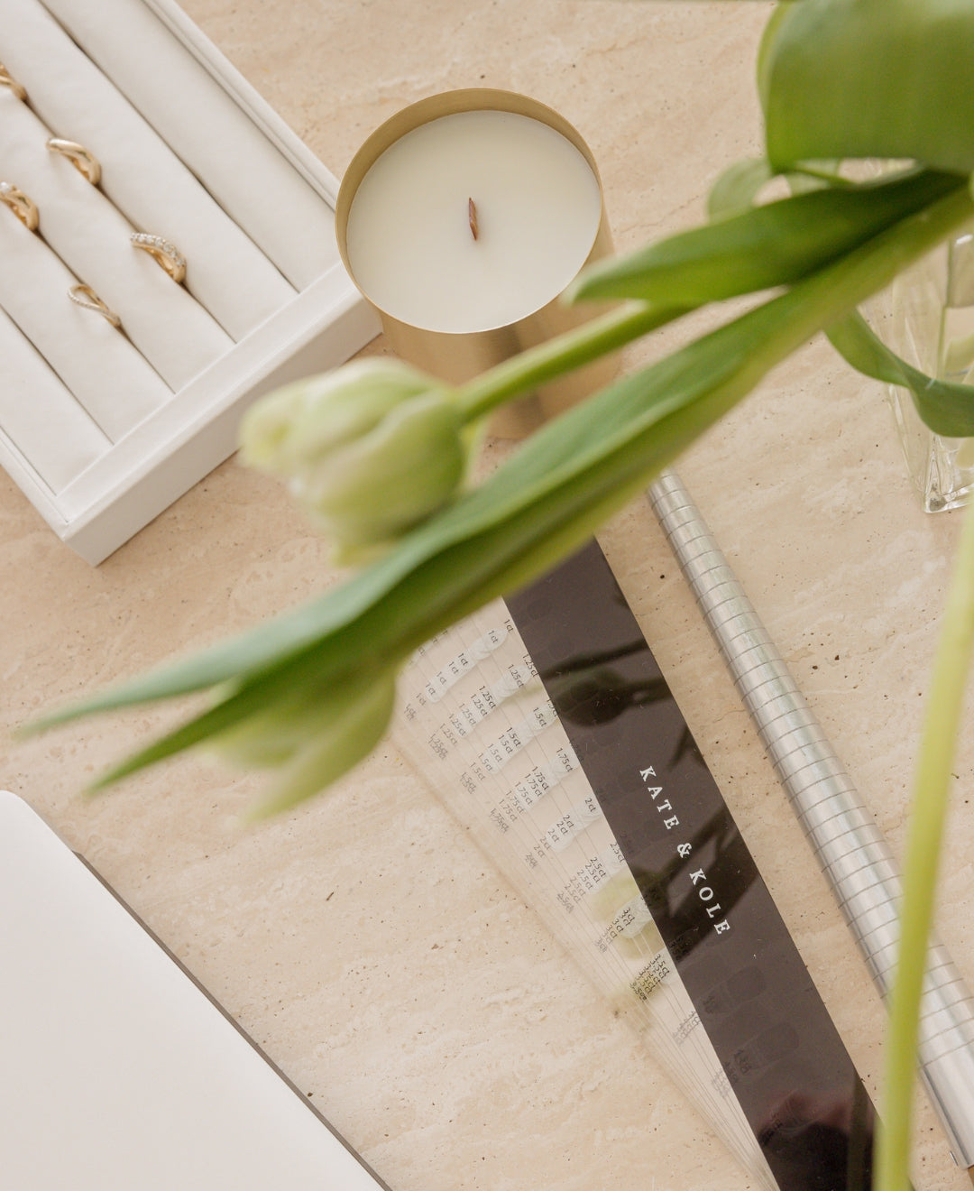 Luxury jewellery setting with elegant rings in a box, a lit candle, and tulips; refined style on a marble surface.