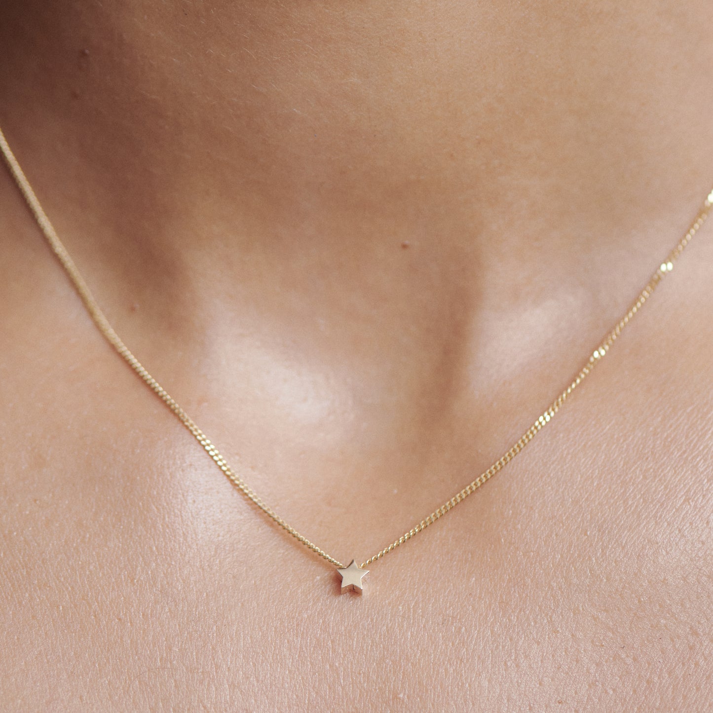 Delicate gold necklace with a tiny star pendant resting on a woman's neck, showcasing luxury jewellery craftsmanship.