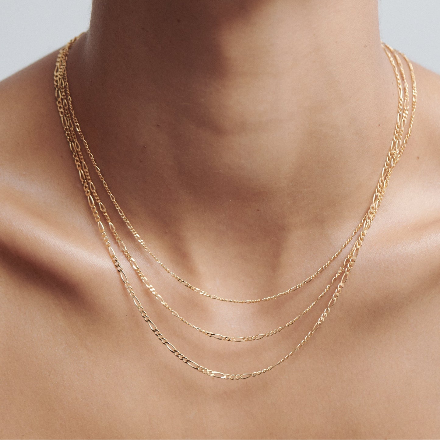 Close-up of a person wearing three delicate gold chains layered elegantly around the neck, showcasing luxury jewellery fashion.
