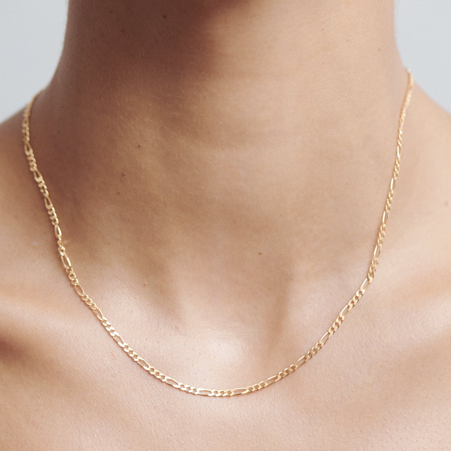 Gold chain necklace on a person's neck, featuring delicate, interlocking links. Simple luxury jewellery style.