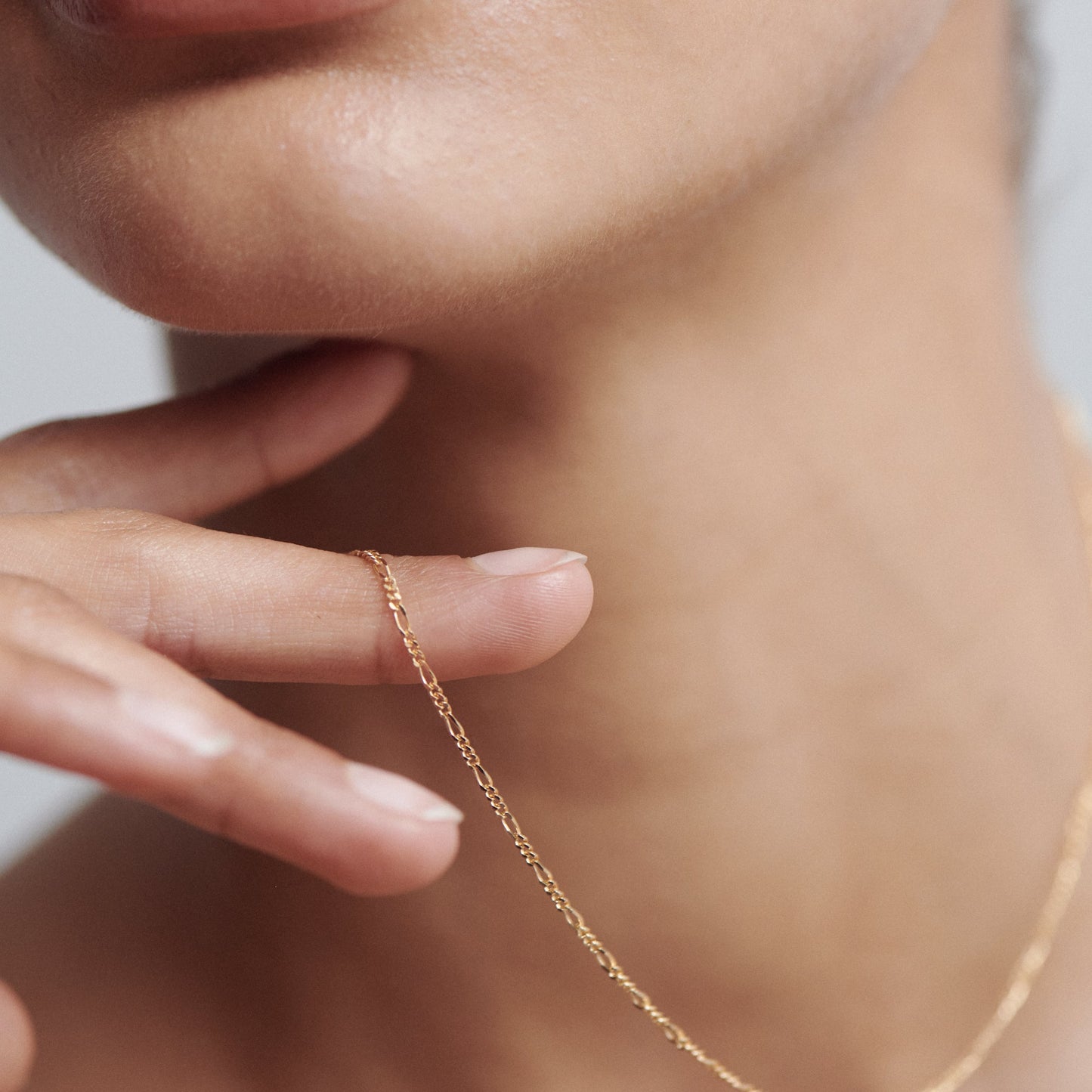 Close-up of a woman's neck and hand, featuring a delicate gold chain necklace draped over her fingers.