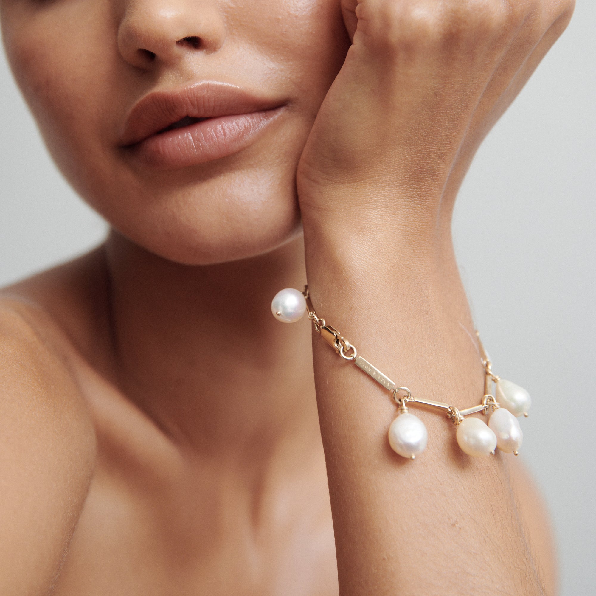 Woman wearing a gold bracelet adorned with white pearl charms, highlighting luxury jewellery. Close-up of her wrist and lower face.