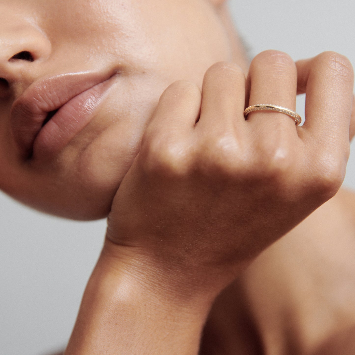 Close-up of a woman's hand, elegantly adorned with a thin, textured gold ring, resting near her lips, exuding luxury and sophistication.