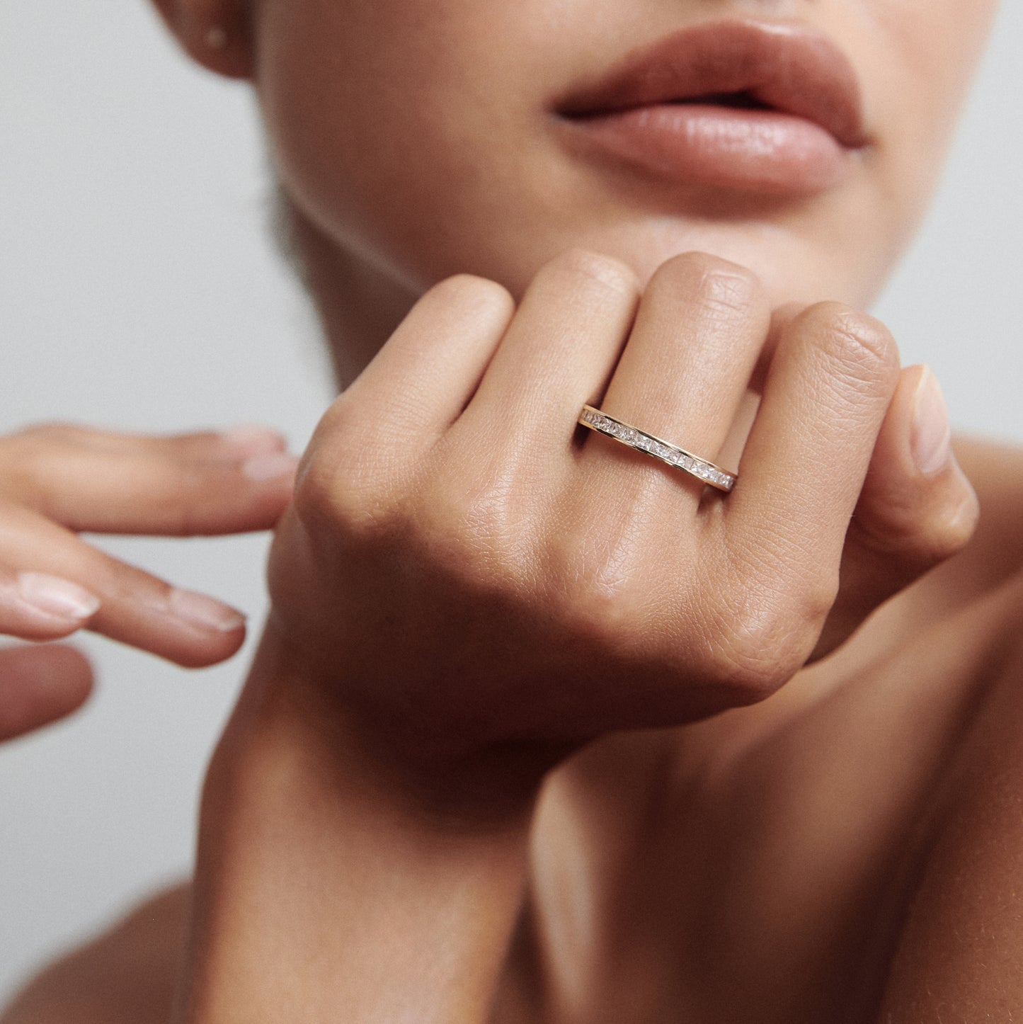 Close-up of a woman's hand wearing a thin diamond-encrusted gold ring. The focus is on the jewellery against a soft, neutral background.