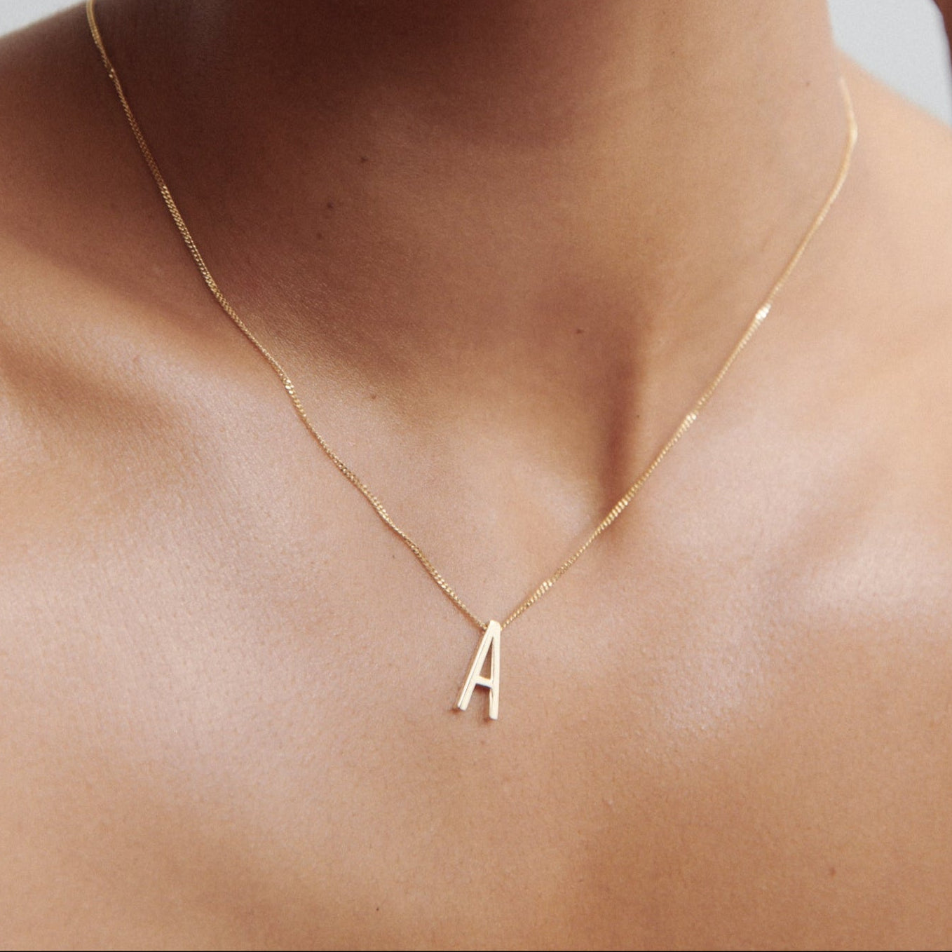 Close-up of a woman wearing a delicate gold necklace with an 'A' pendant, showcasing minimalist luxury jewellery.
