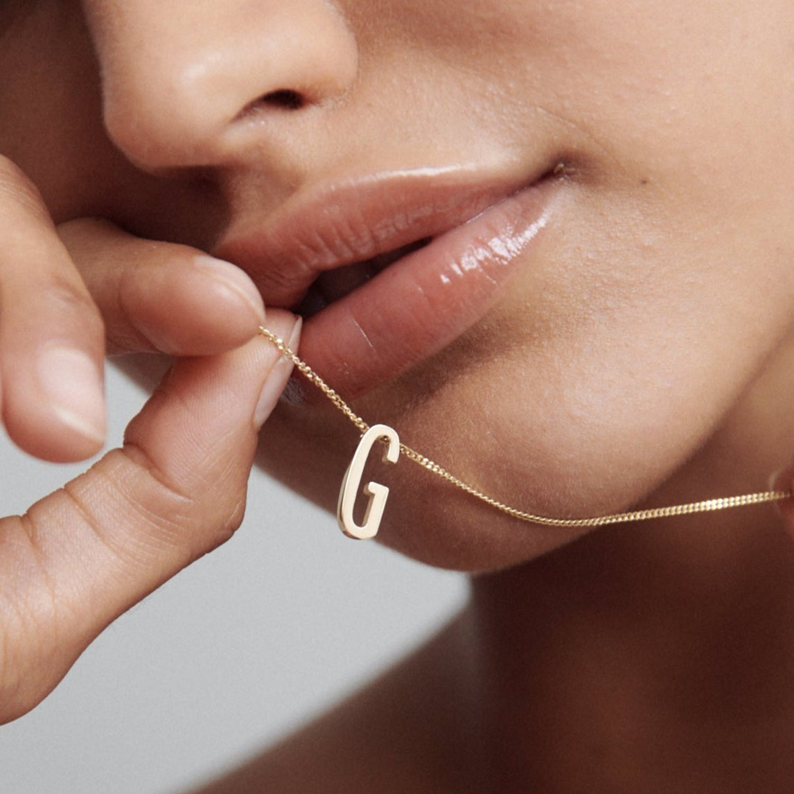 Close-up of a woman holding a gold necklace with a “G” pendant near her lips, highlighting luxury jewellery and elegant design.