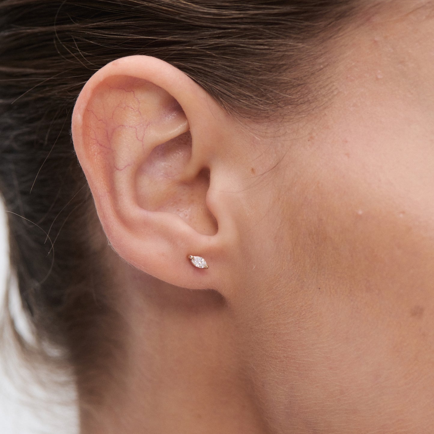 Close-up of an ear wearing a small marquise-cut diamond stud earring, highlighting luxury jewellery detail and elegance.