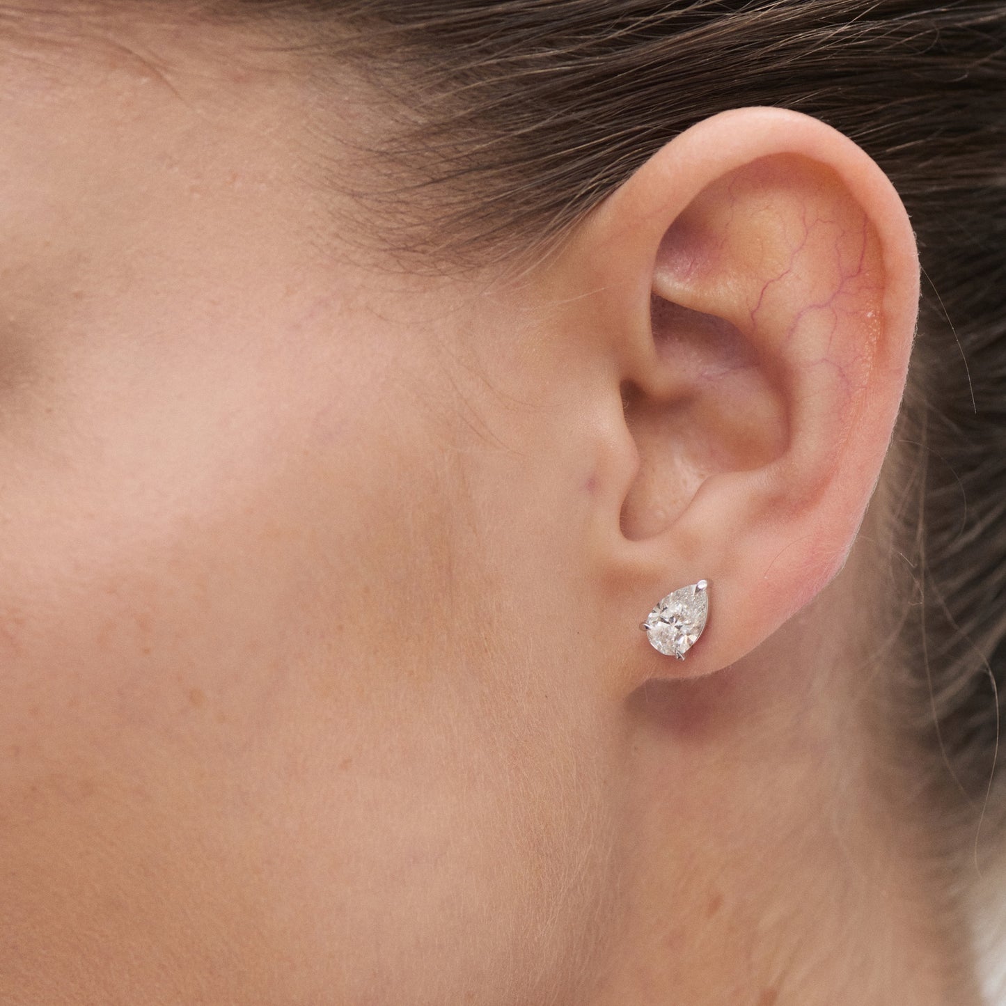 Close-up of a woman's ear wearing a pear-shaped diamond stud earring, showcasing luxury jewellery elegance.