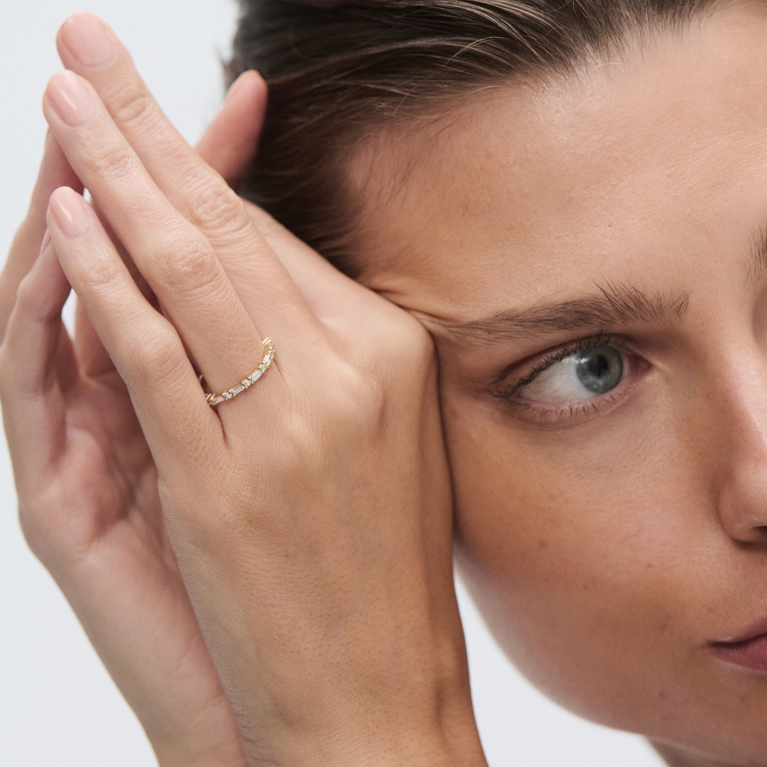 Close-up of a person holding their face, wearing a delicate gold band on their finger. Luxurious and minimalist jewellery style.