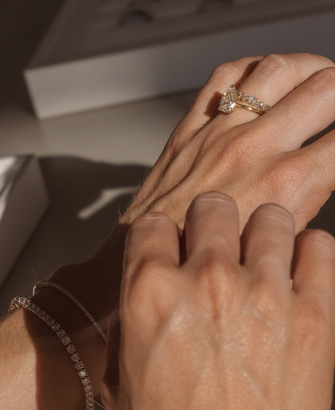 Close-up of hands showcasing a luxurious diamond ring and bracelet set in warm lighting, emphasising high-end jewellery elegance.