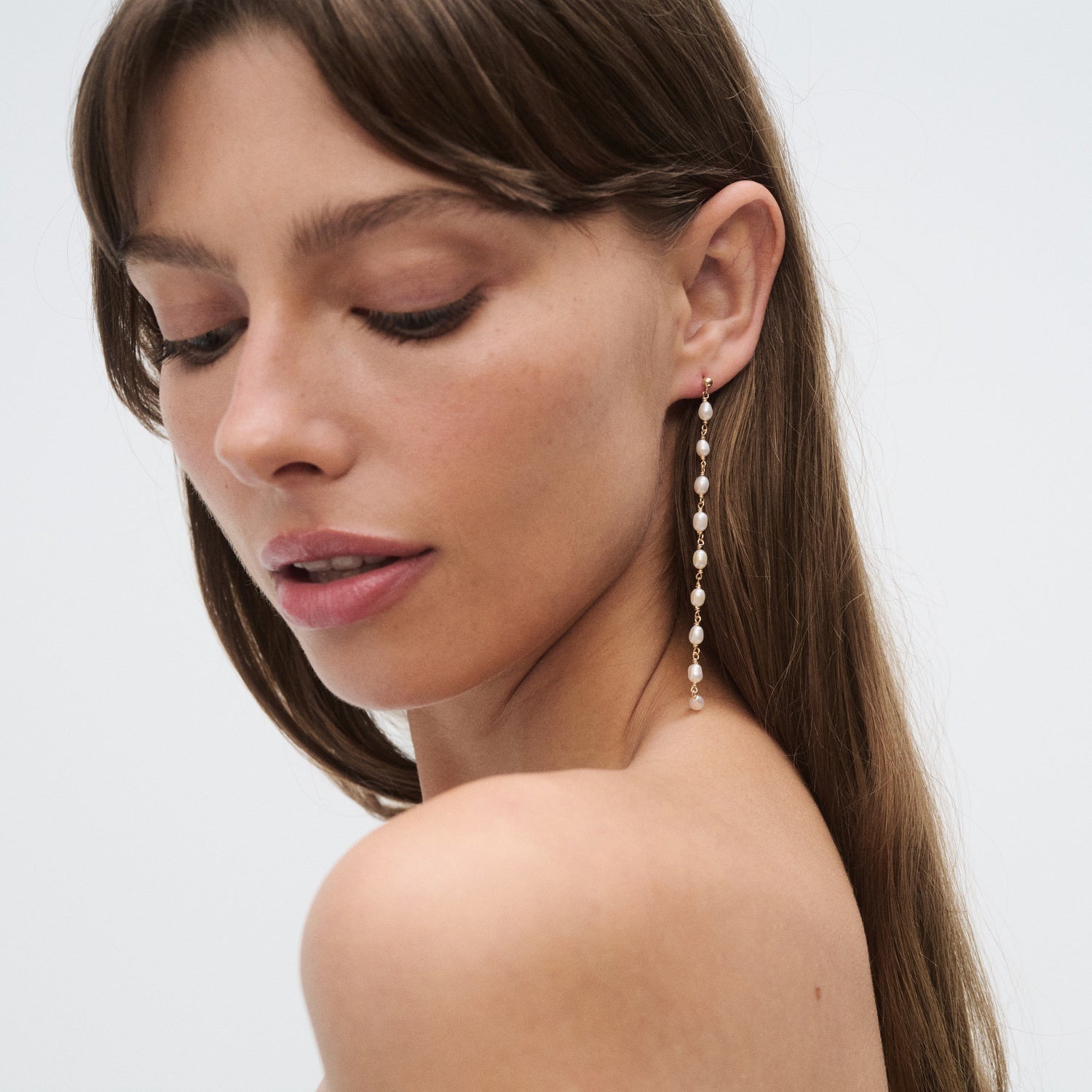 Woman wearing a long, elegant pearl earring, with a serene expression. Luxurious jewellery on display, accentuating her natural beauty.