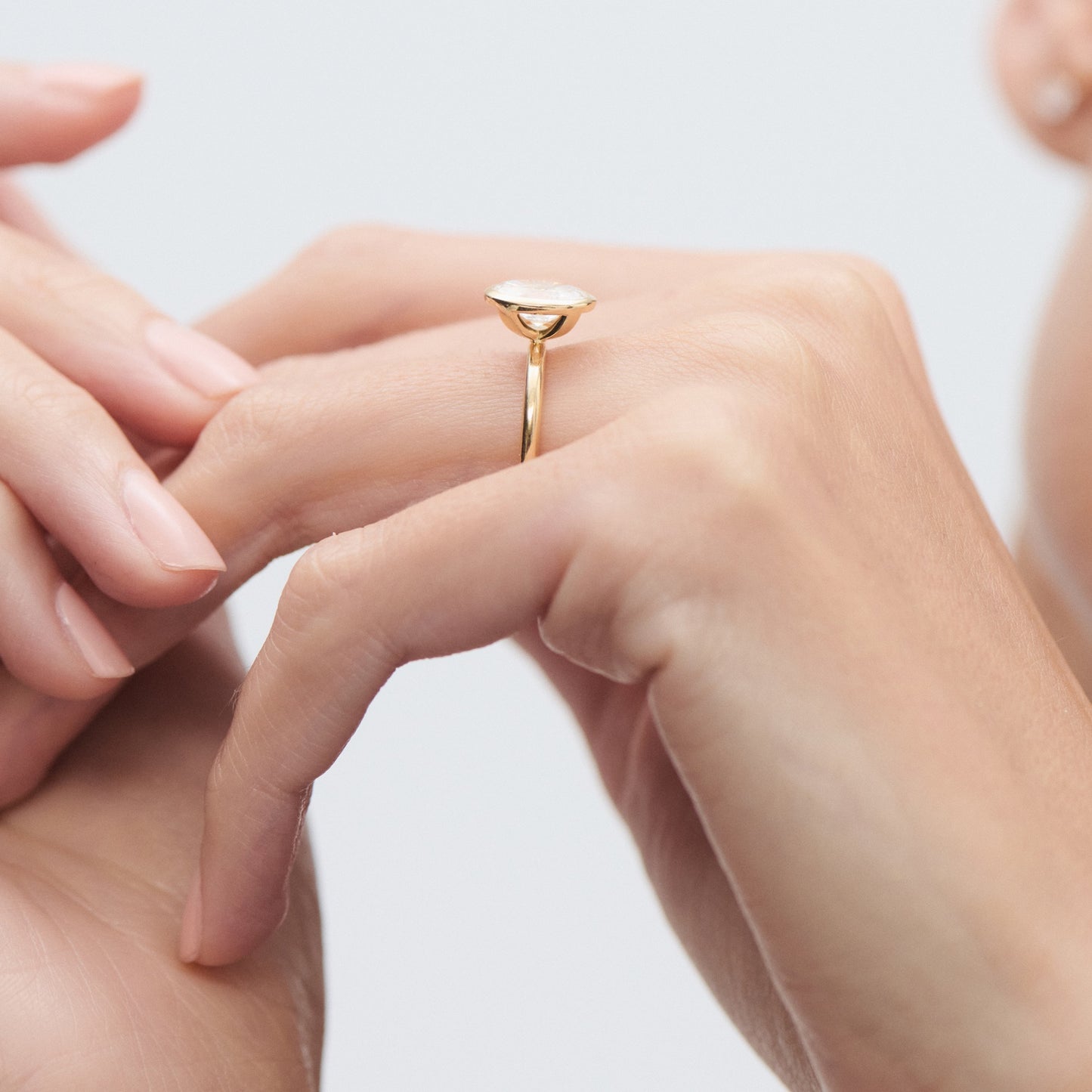 A person's hand elegantly displays a sleek gold ring with a curved design against a light background.