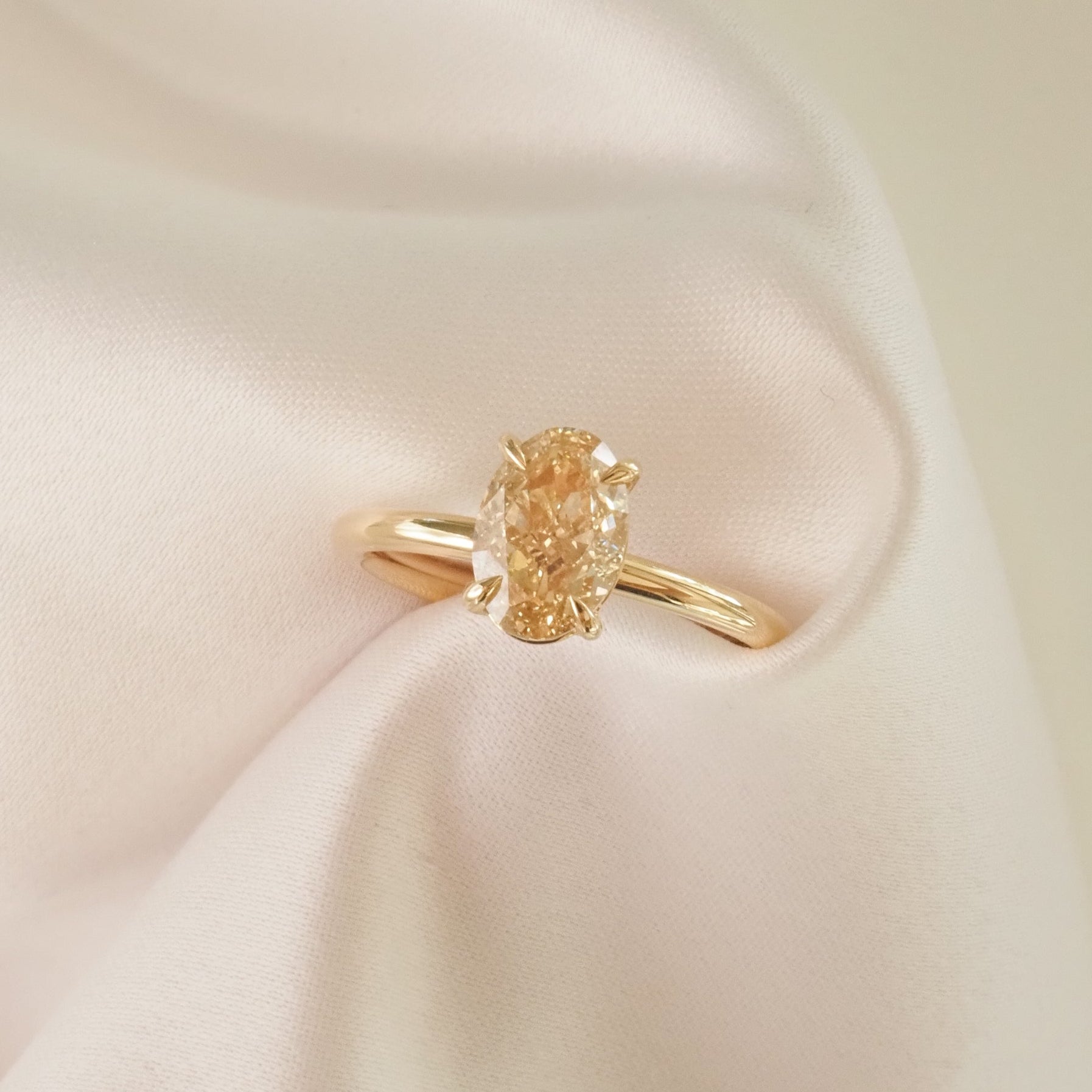 Gold ring with an oval-cut yellow diamond, elegantly displayed on soft, white fabric, highlighting its luxury and elegance in jewellery design.