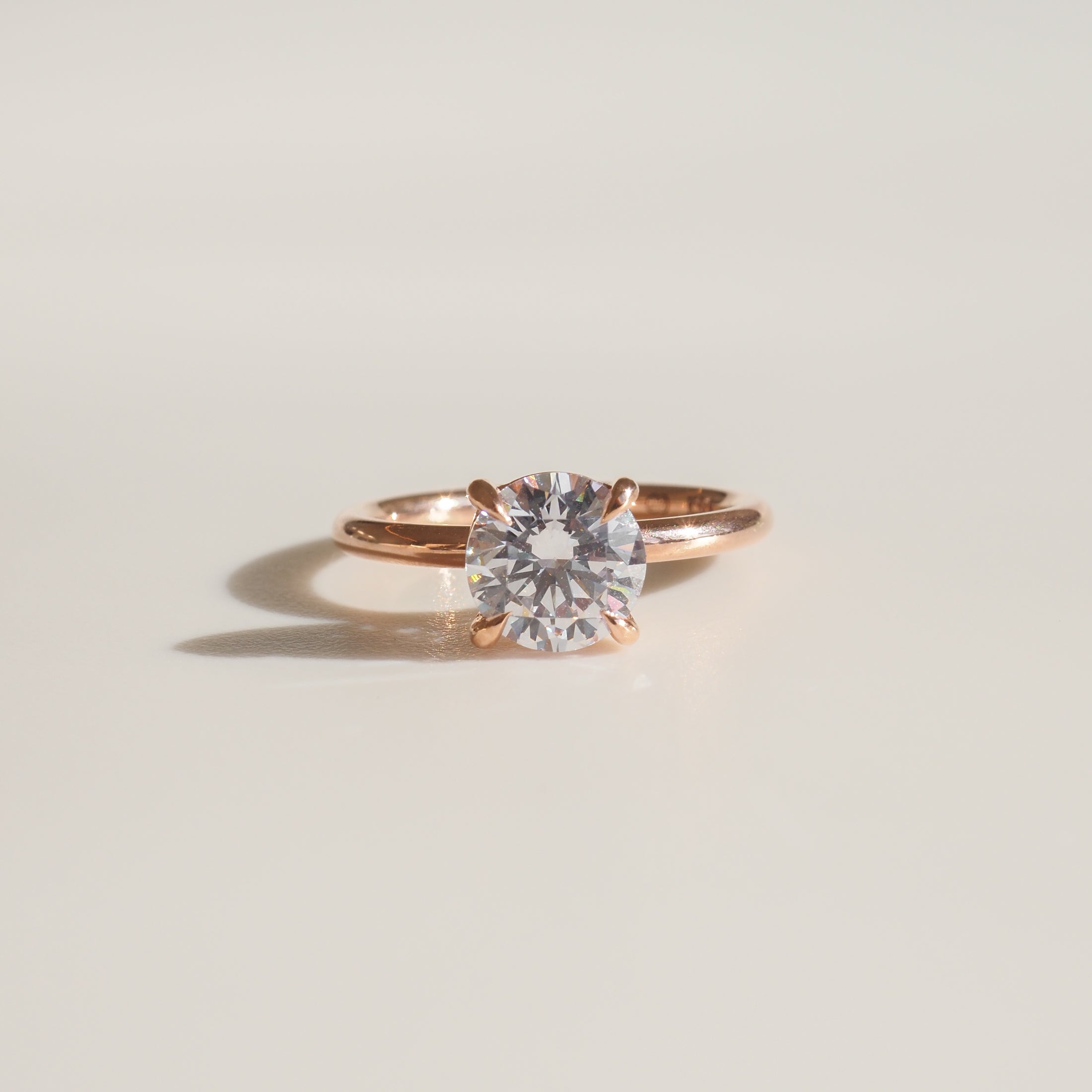 Rose gold solitaire ring with a round diamond, elegantly displayed on a light background. Luxurious and classic jewellery piece.