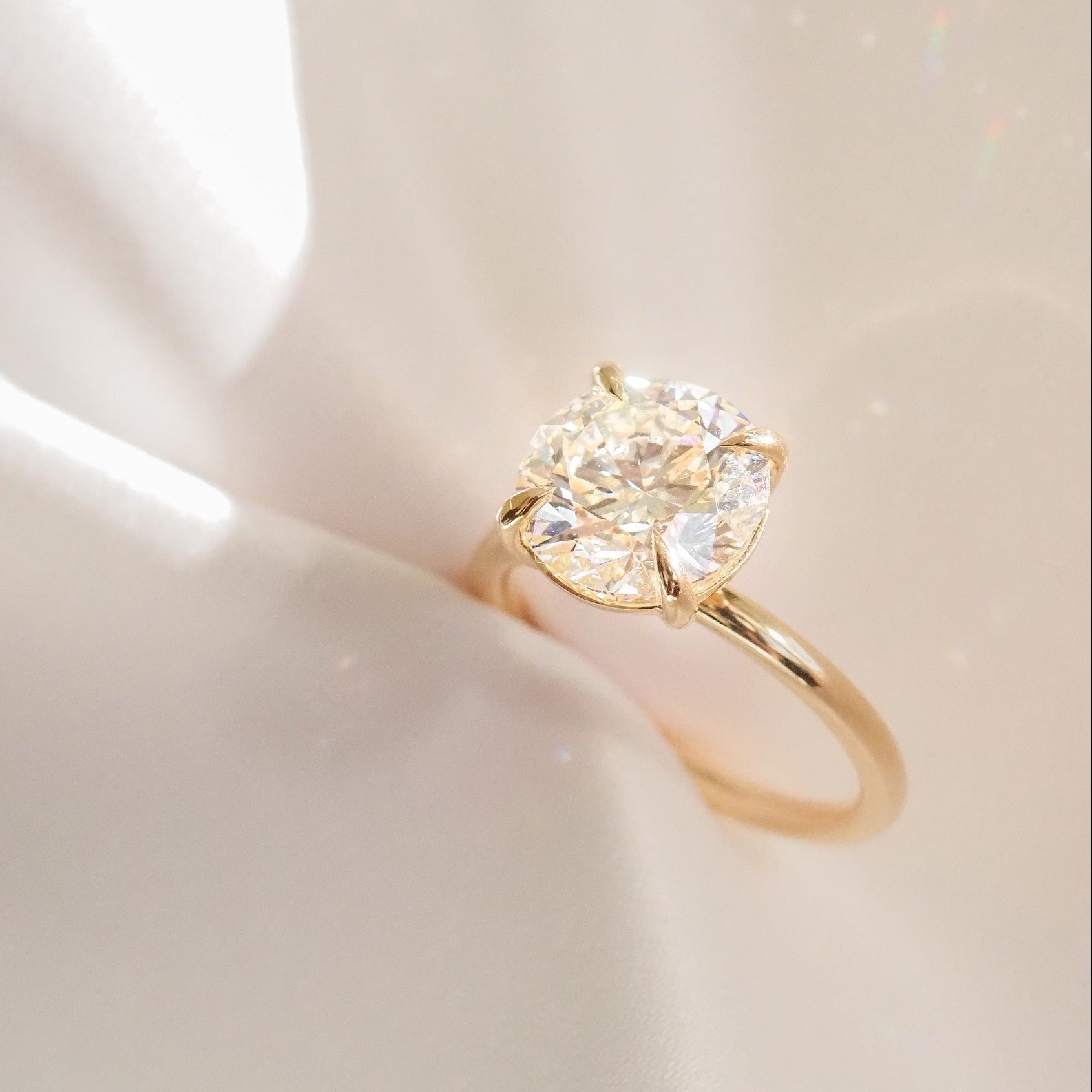 Gold engagement ring with a large round diamond, elegantly displayed on a reflective surface casting soft, radiant light patterns.