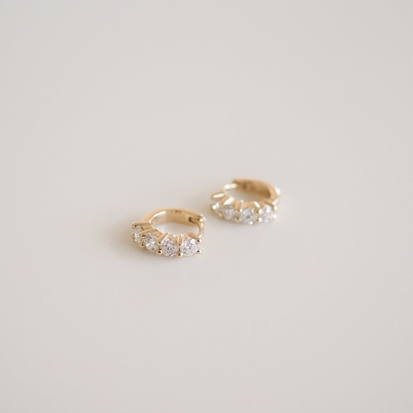 Gold hoop earrings with small diamonds on a light gray background