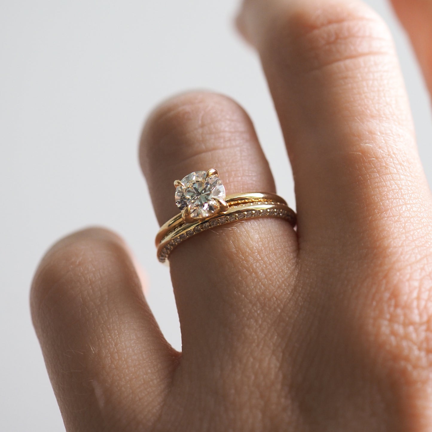 Close-up of a hand wearing a gold engagement ring with a large diamond, paired with a gold band. Luxurious jewellery style.