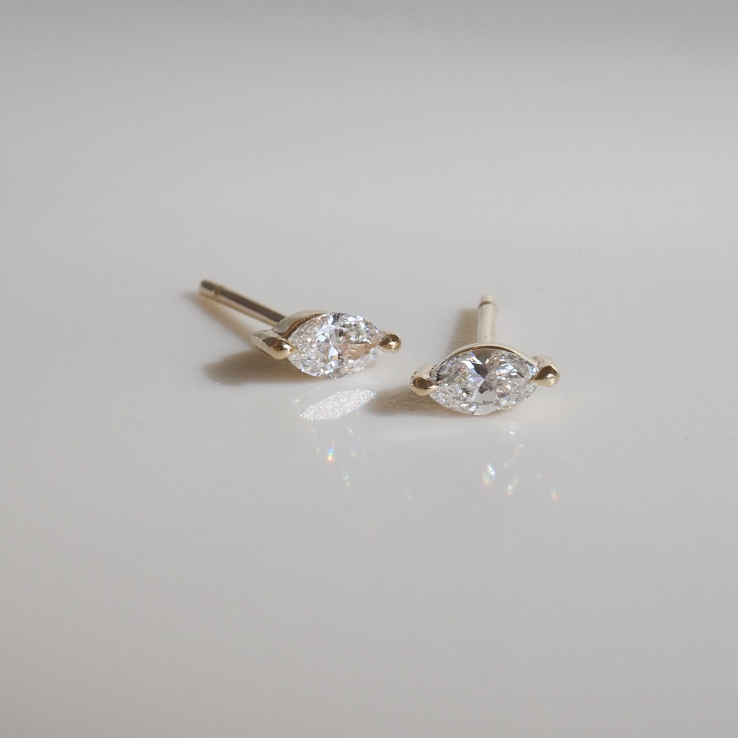 Marquise diamond stud earrings set in gold, elegantly displaying their brilliance on a smooth, light surface.