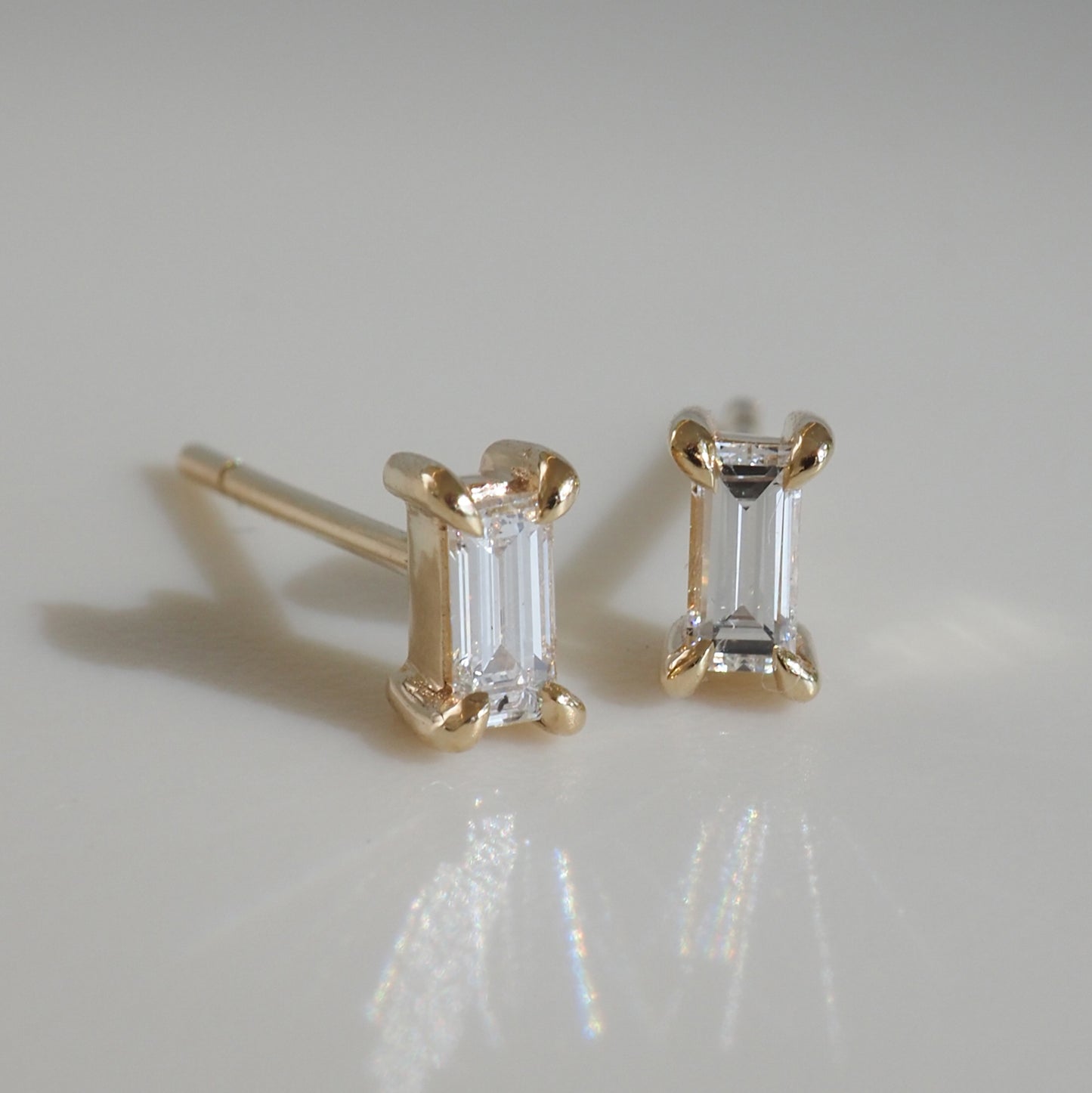 Gold earrings with emerald-cut diamonds on a light background; luxury jewellery piece reflecting light with elegance.