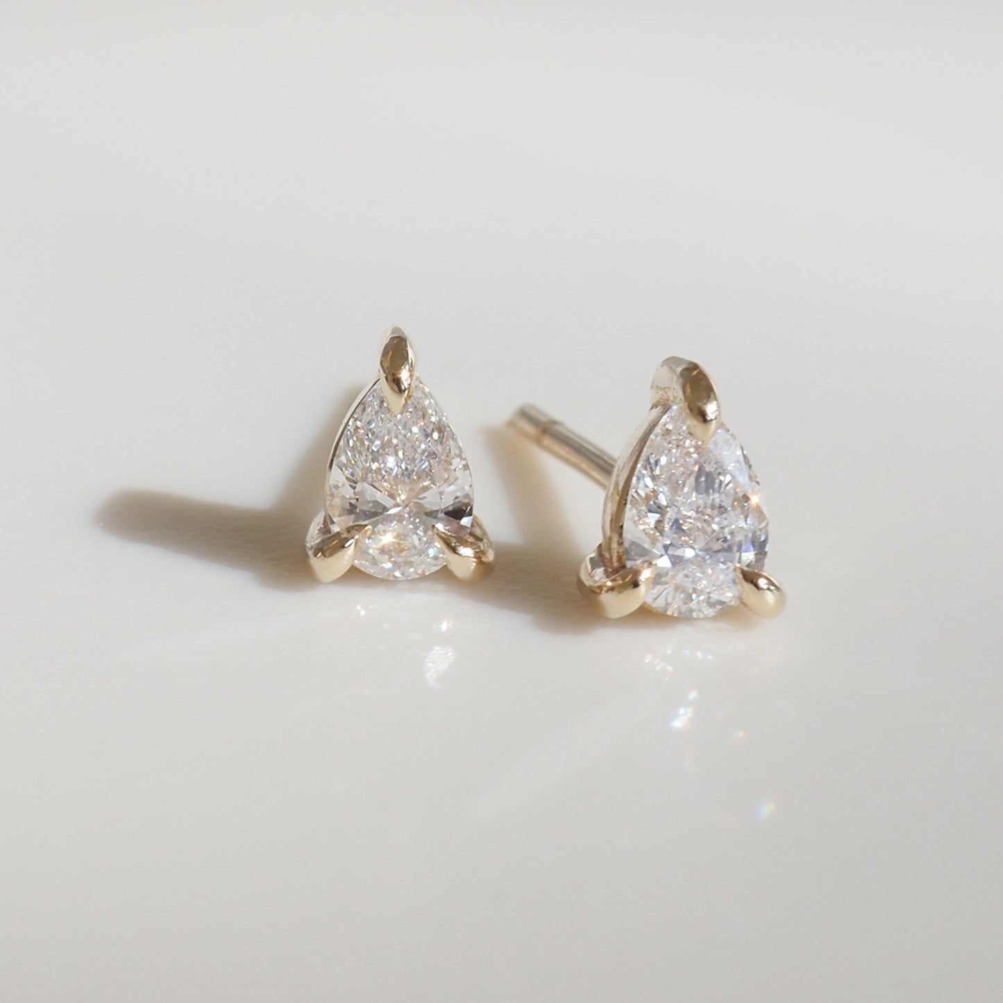 Pear-shaped diamond earrings set in gold, displayed on a soft white background, showcasing luxury and elegance.