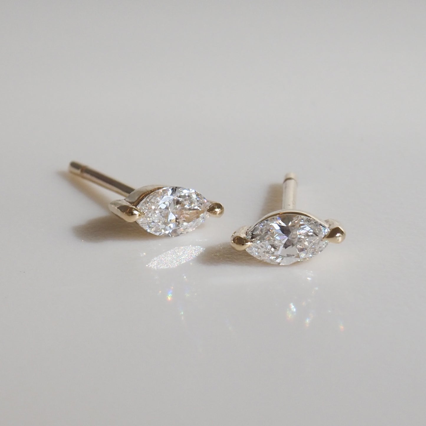 Pair of marquise diamond stud earrings set in yellow gold, placed on a light grey surface. Luxurious and elegant jewellery design.