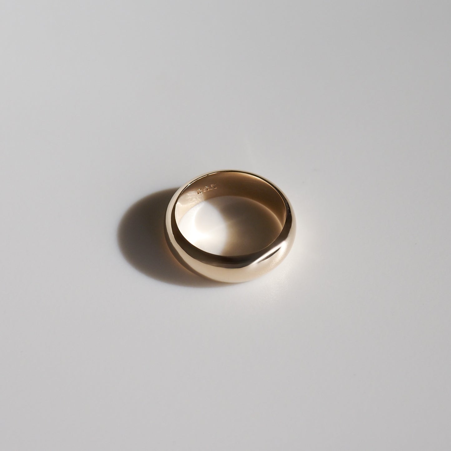 High-end polished gold ring on a light grey background, showcasing a classic design and luxury jewellery appeal.