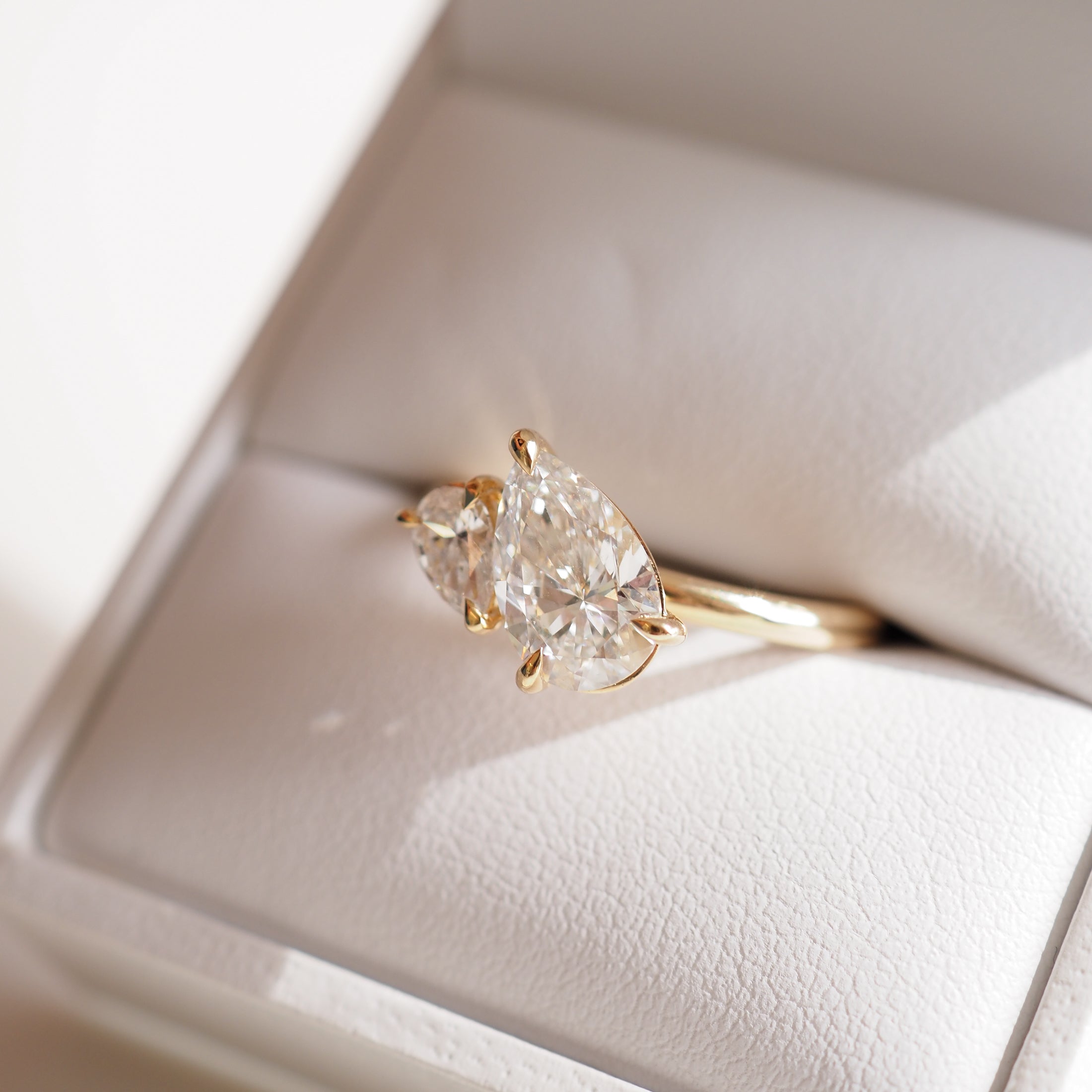 Pear-shaped diamond ring in gold setting, displayed in a white jewellery box, capturing elegant luxury.