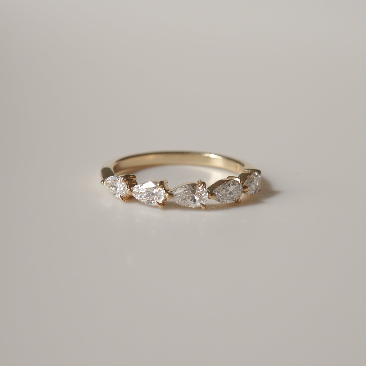 Gold ring with five pear-shaped diamonds set in a row, displayed on a neutral background. Luxury jewellery, elegant design.