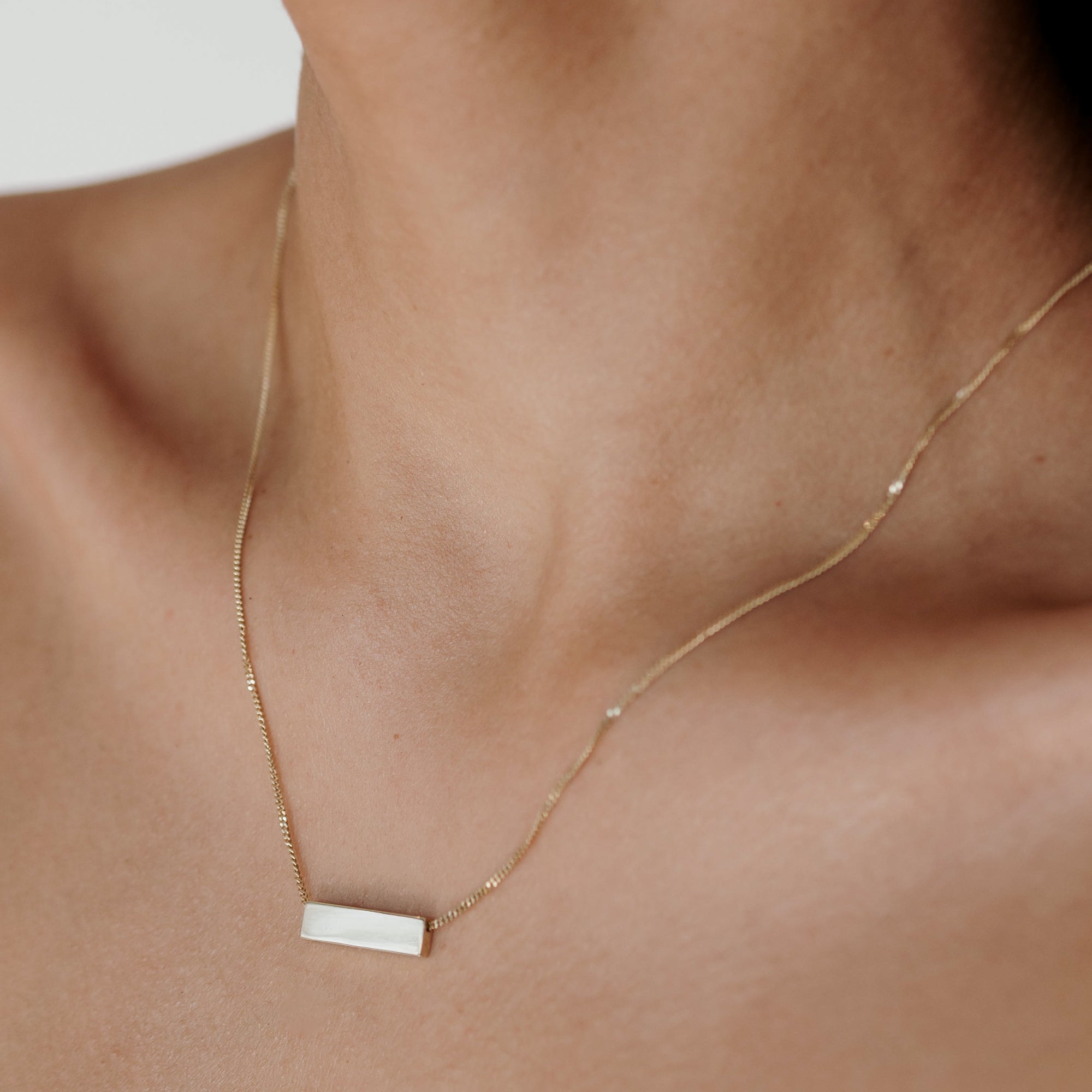 Close-up of a woman's neck adorned with a minimalist gold necklace featuring a rectangular white pendant, showcasing luxury jewellery details.