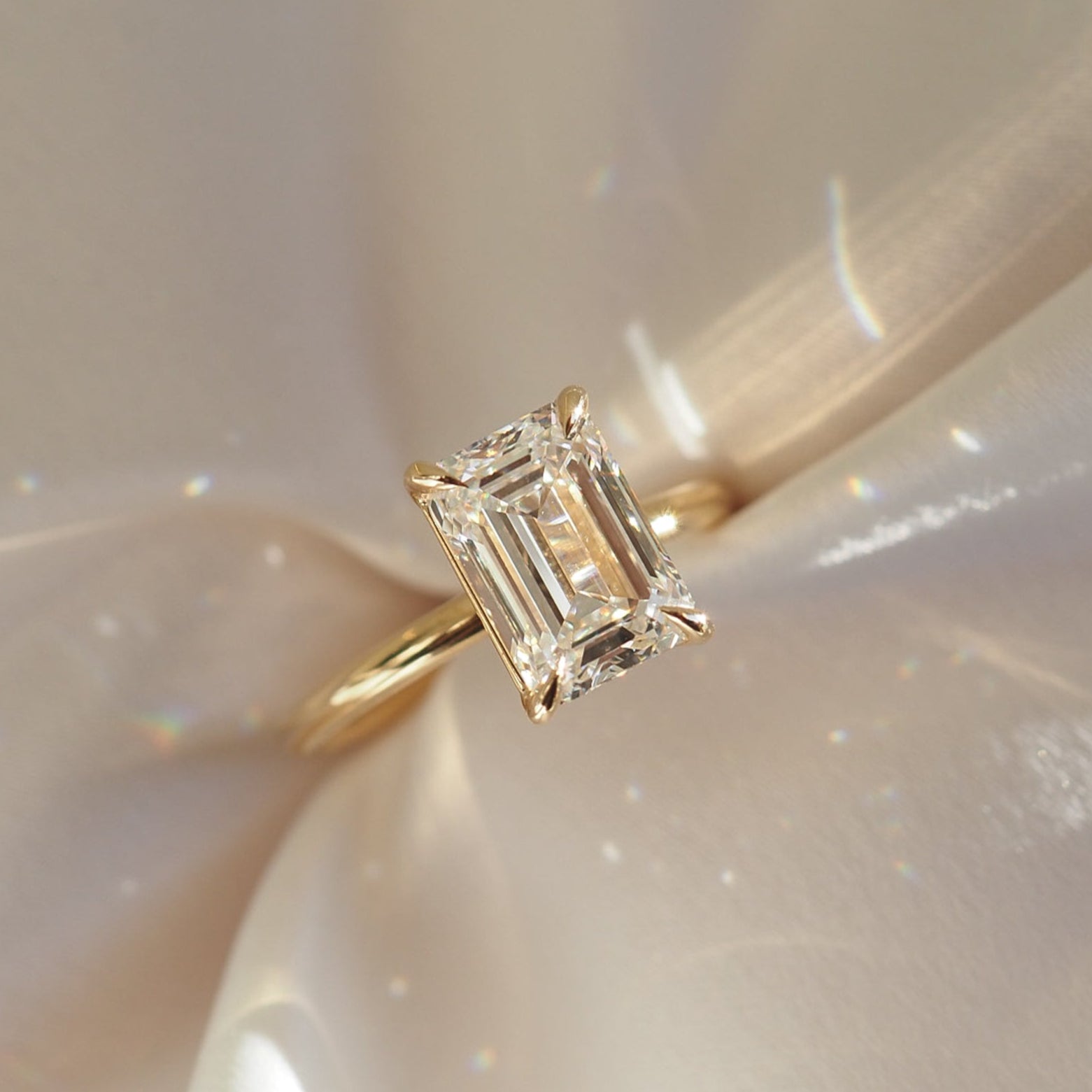 Emerald cut diamond ring with a gold band on a soft, shimmering fabric background. Luxurious, elegant jewellery design.