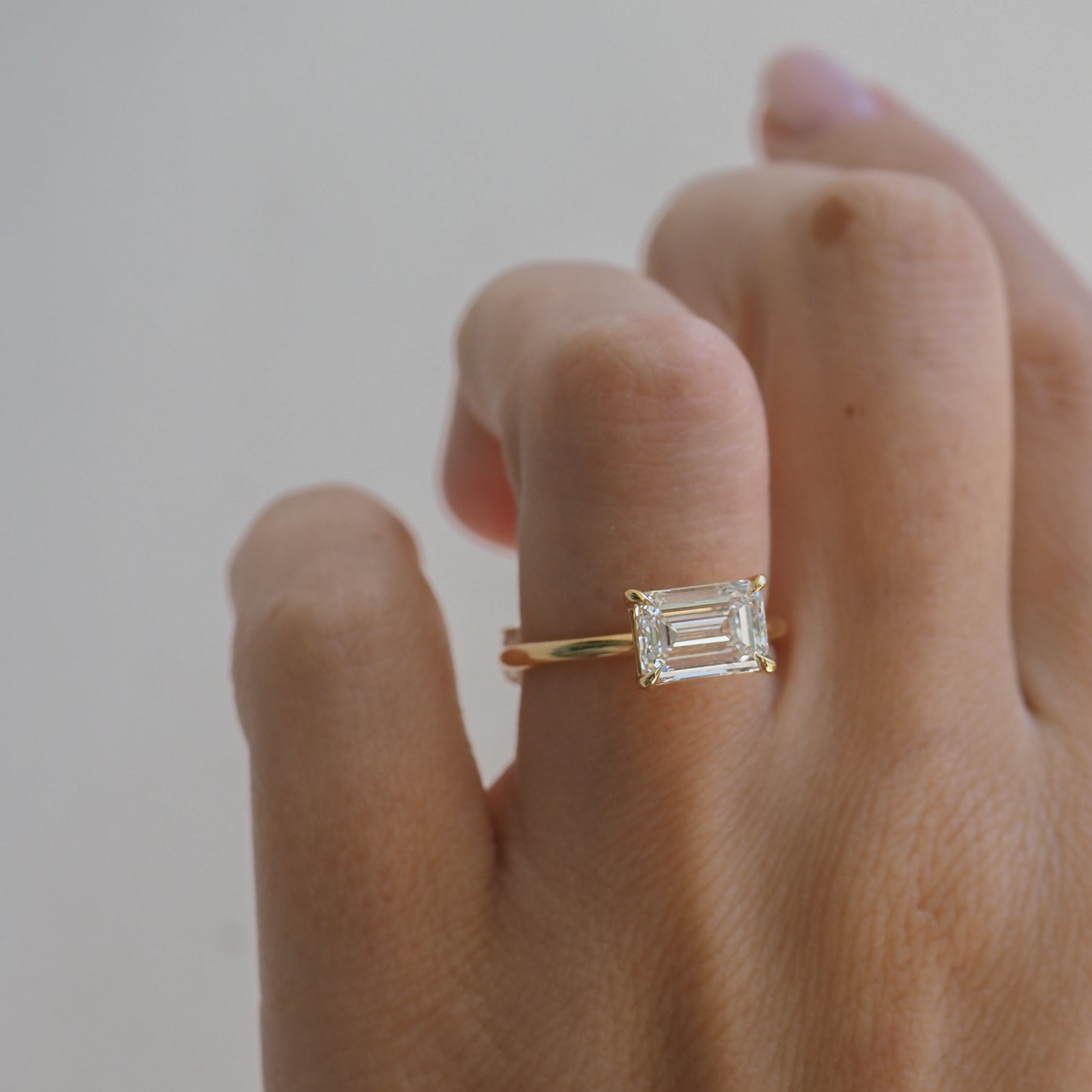 Emerald-cut diamond ring on a hand with a simple gold band, showcasing elegance and luxury jewellery design.