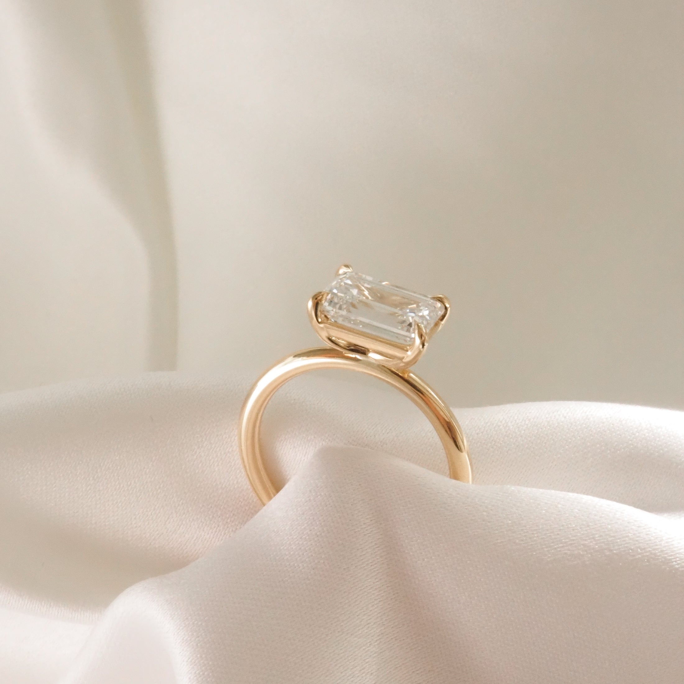 Emerald-cut diamond ring with gold band displayed on silky cream fabric, exuding elegance and luxury in fine jewellery design.