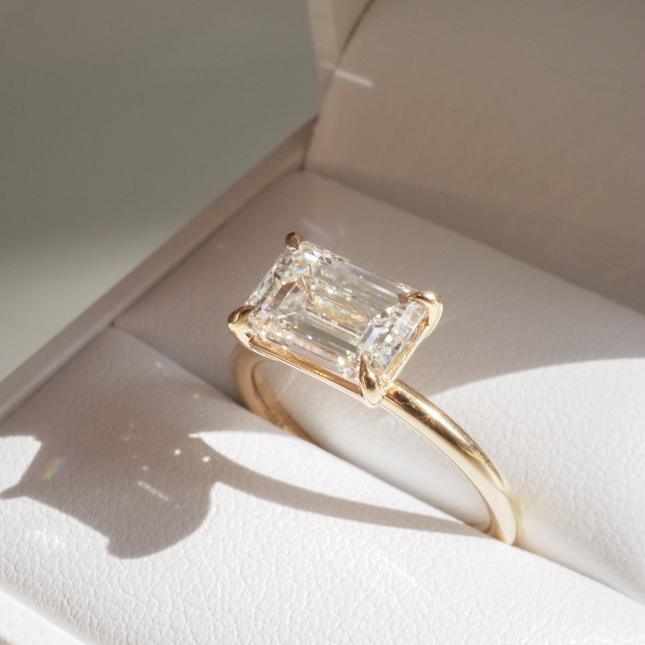 Emerald-cut diamond ring in a gold setting displayed in an elegant jewellery box, capturing natural light and shadows.
