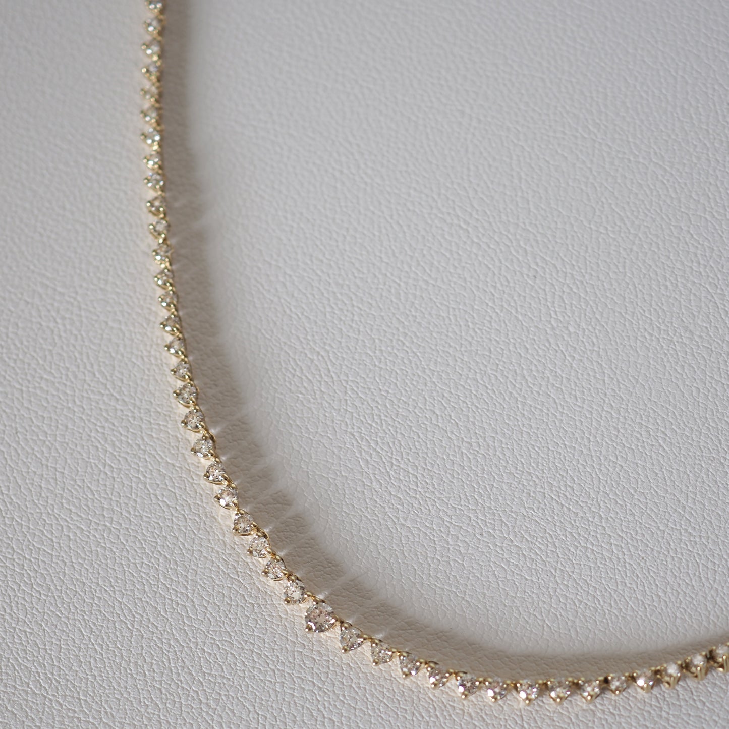 Gold diamond tennis necklace on a white leather surface, showcasing elegant, luxury jewellery design.