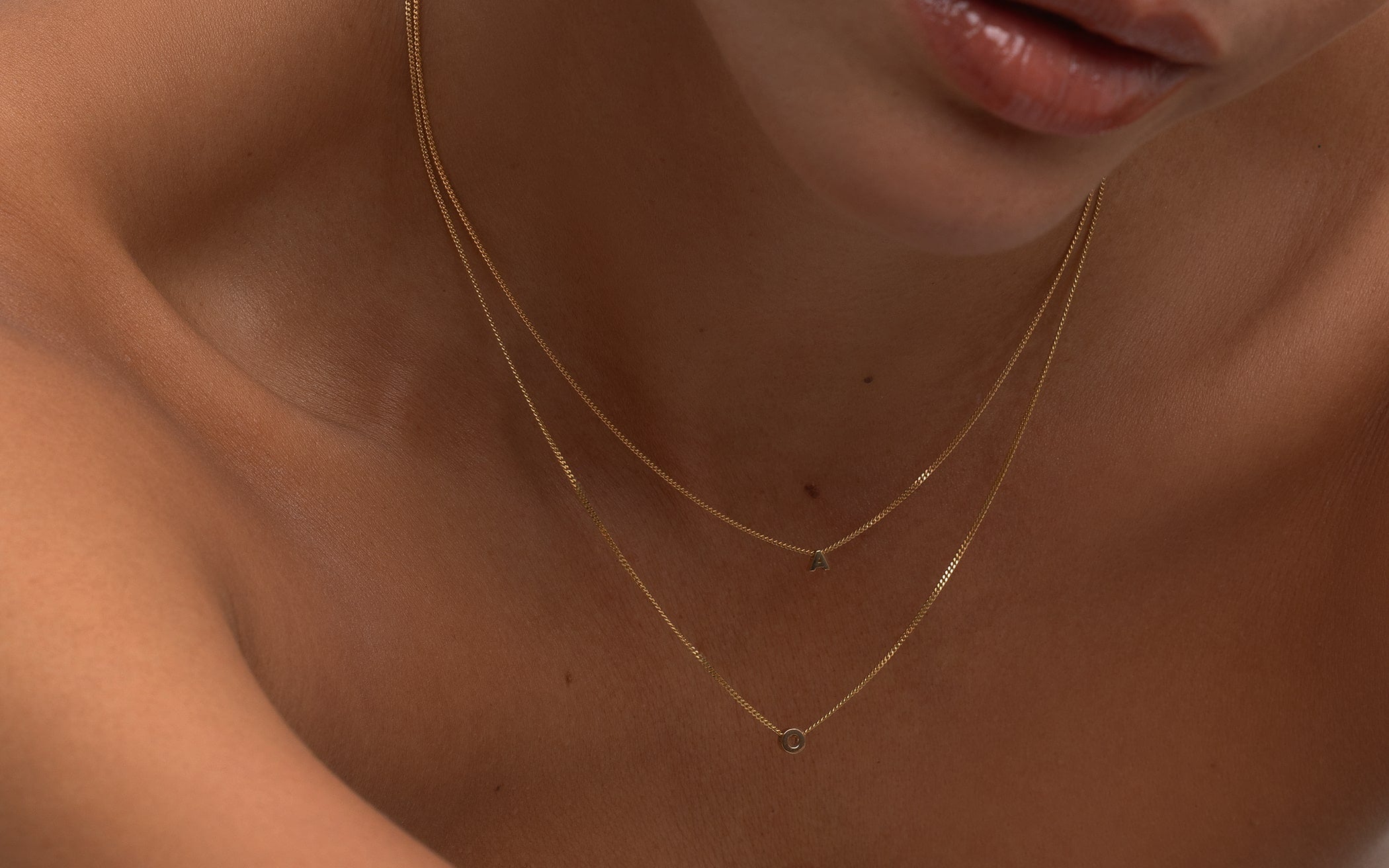 Close-up of a person wearing a delicate gold necklace with small letter pendants.