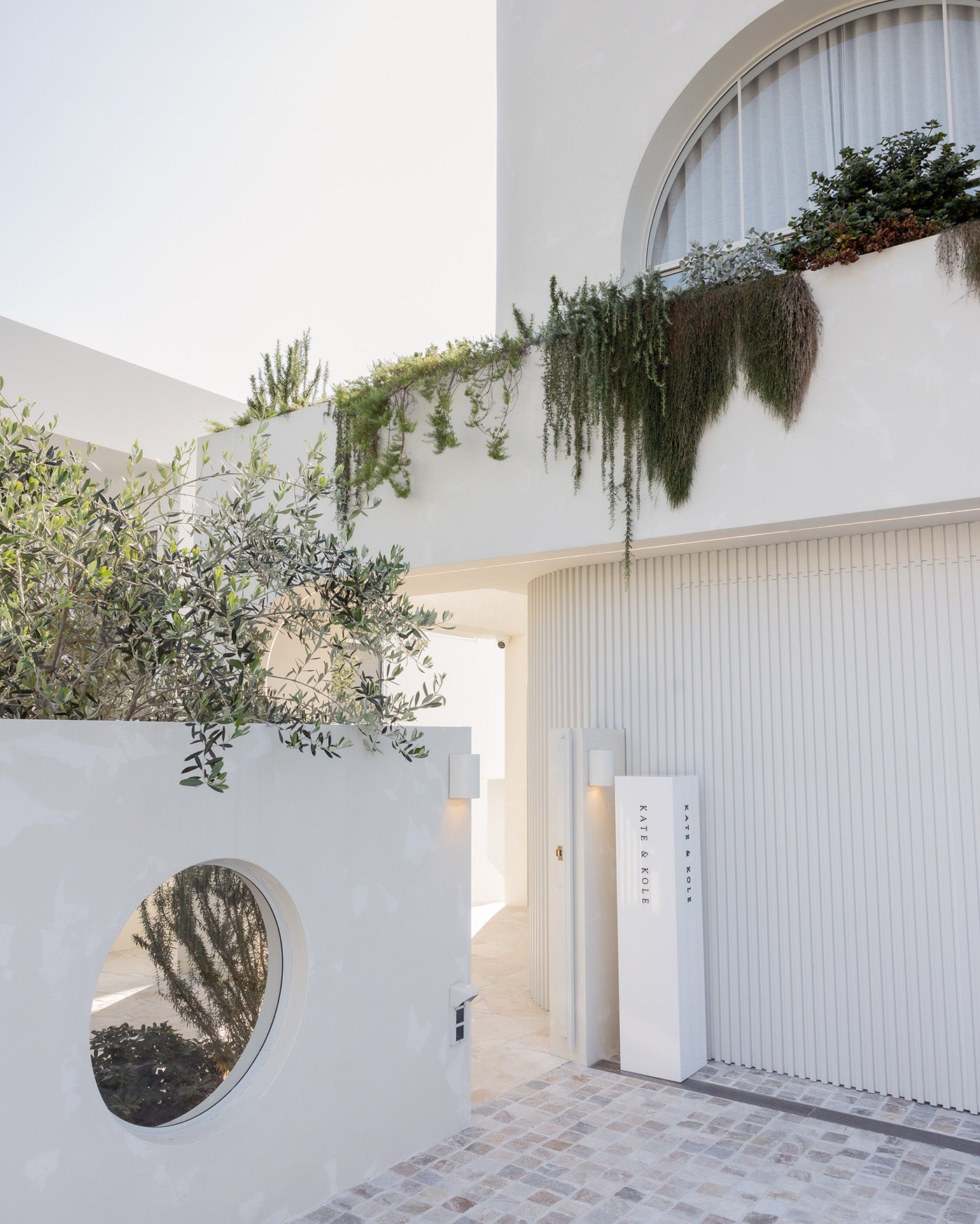Modern luxury boutique entrance with white minimalist design, hanging greenery, and a circular window, conveying elegance and sophistication.
