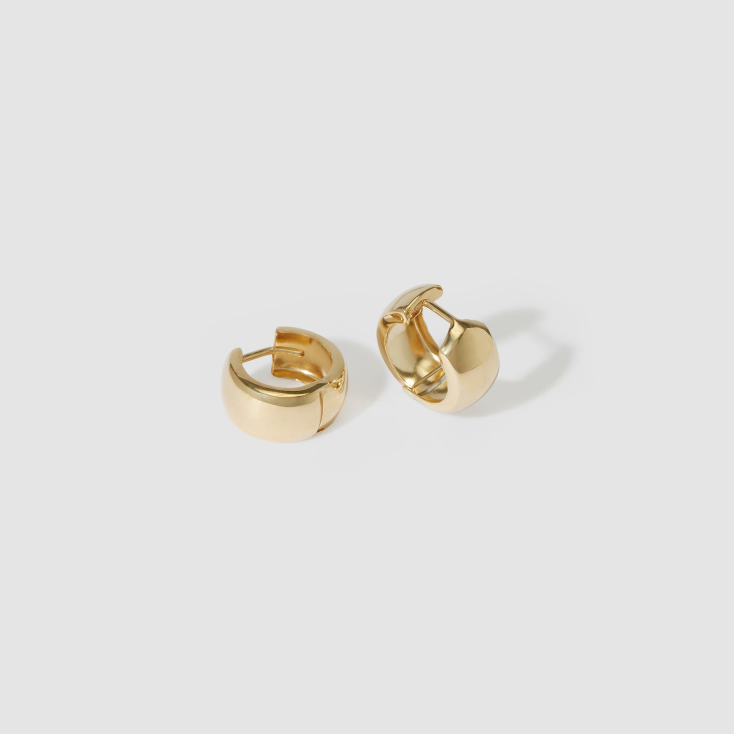 Gold hoop earrings on a white background, featuring a thick, rounded design. Luxurious and elegant, ideal for a high-end jewellery collection.