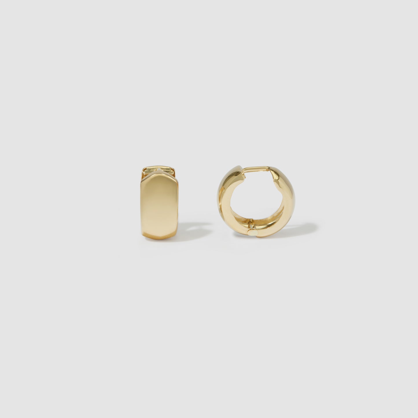 Gold huggie hoop earrings on white background, showcasing minimalist luxury jewellery design. One earring is closed, the other is open.