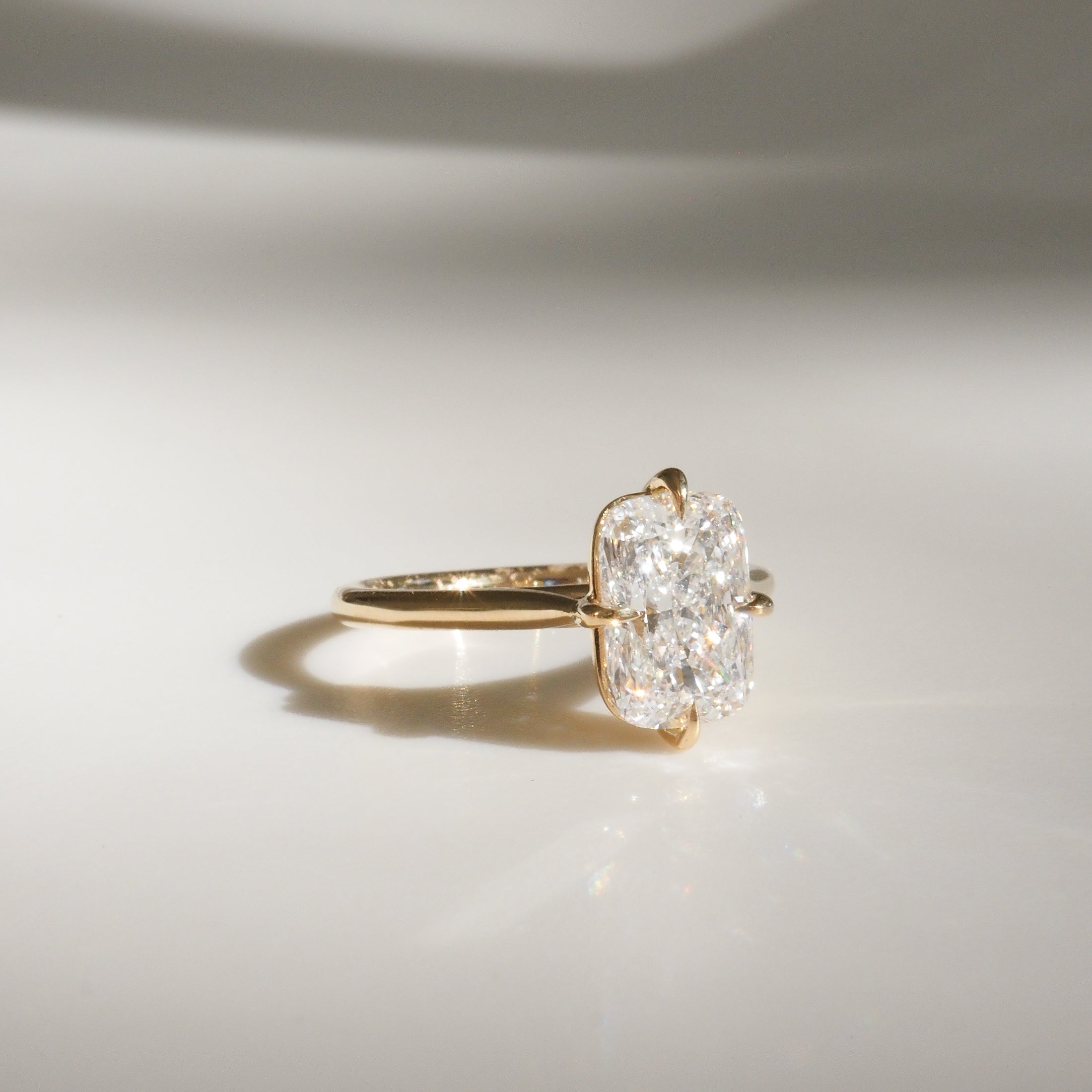 Gold ring with a radiant-cut diamond solitaire, elegantly displayed on a reflective surface, showcasing luxury jewellery design.