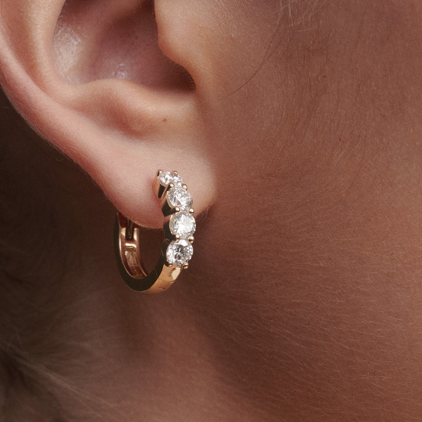 Gold hoop earring with clear stones worn on an ear