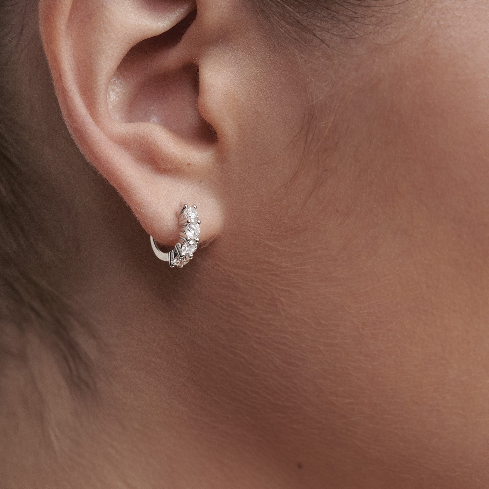 Close-up of an ear wearing a diamond earring on a neutral background