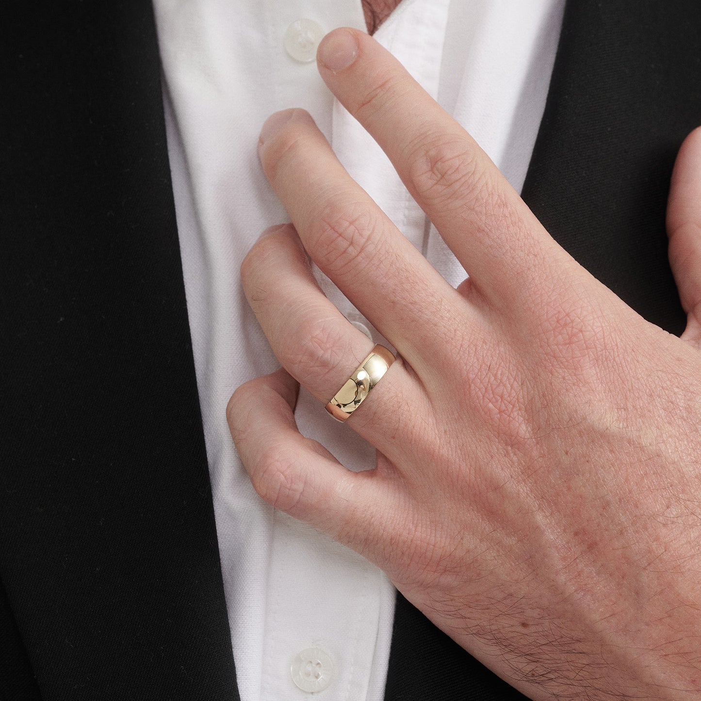 Hand wearing a gold ring with a white shirt and black jacket in the background