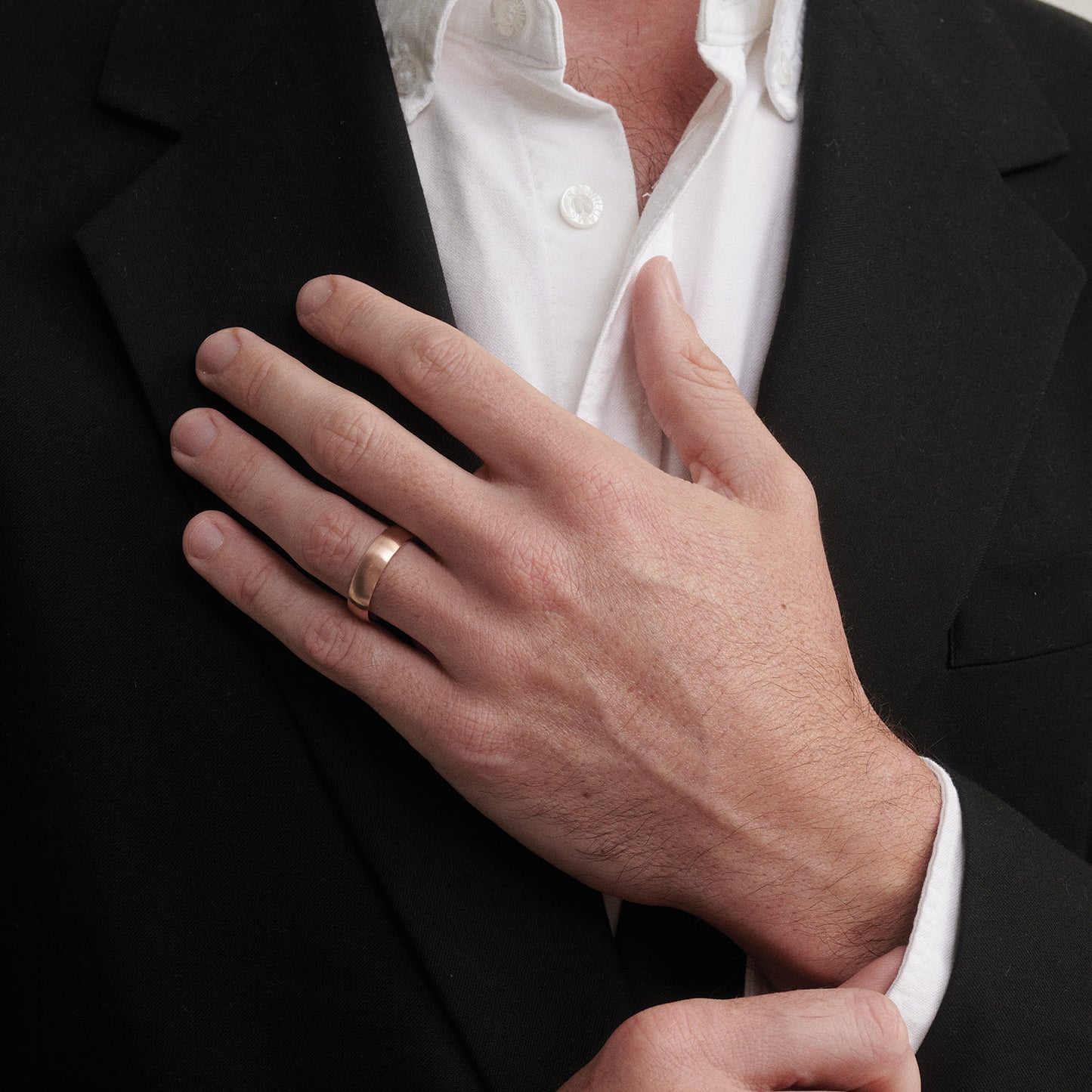 Hand wearing a rose gold ring with a black suit and white shirt in the background