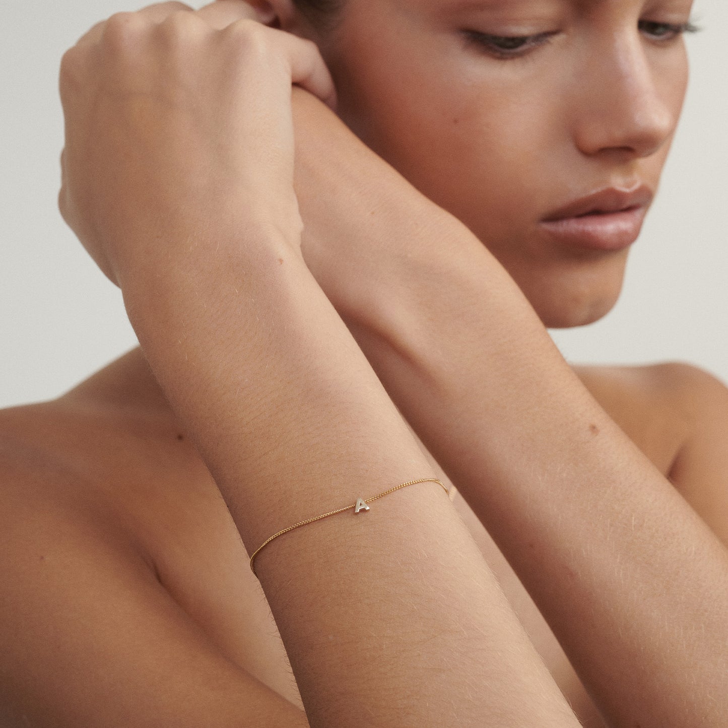 Woman wearing a delicate gold bracelet on a neutral background