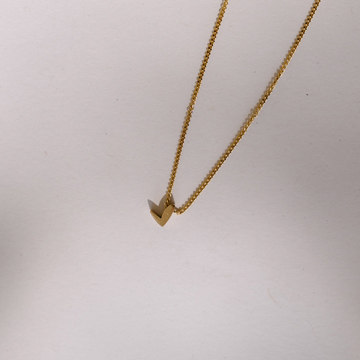 Elegant gold necklace with minimalist V-shaped pendant on a fine chain, set against a plain background.