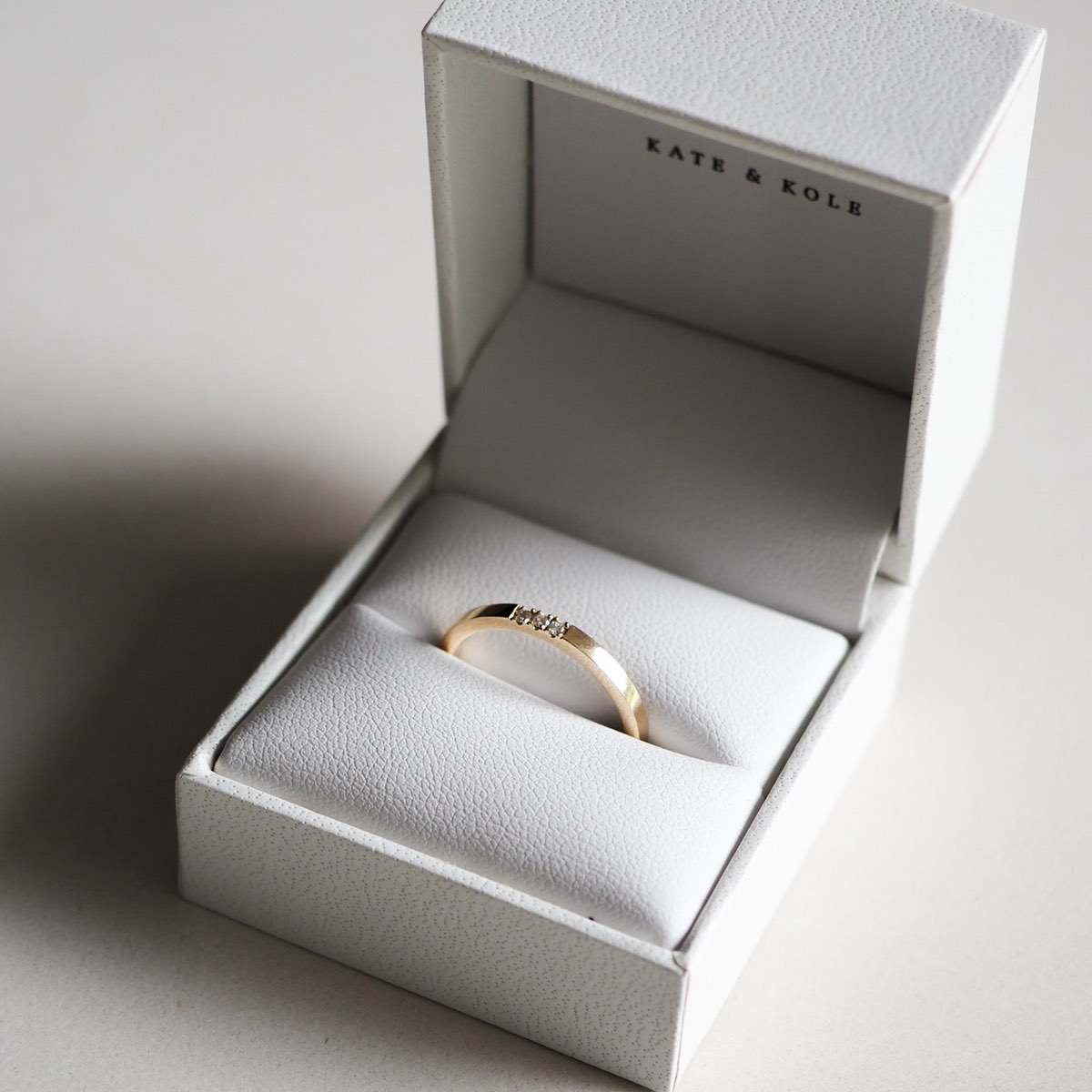 Gold ring with small diamonds in a white Kate & Kole jewellery box on a light surface, showcasing luxury and elegance.